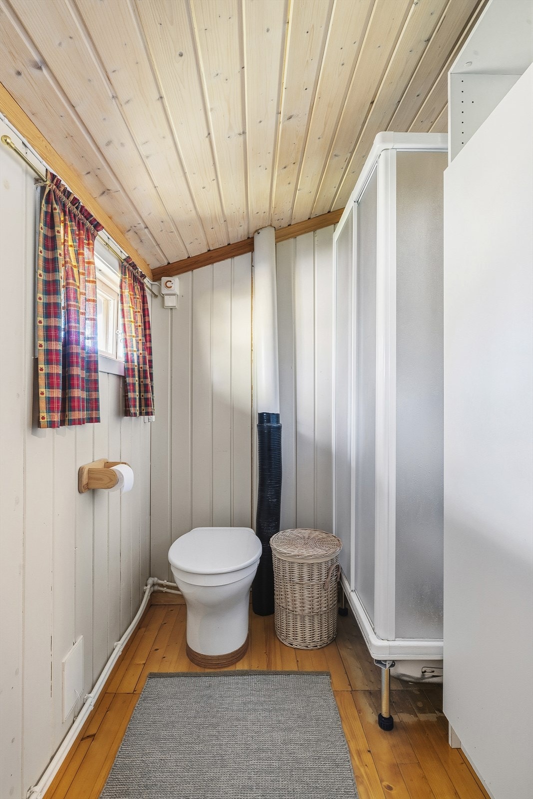 Bad med furugulv og panel på vegger inneholder innredning med vask og speil, dusjkabinett samt formullingstoalett med kammer for avfall. Galleribilde