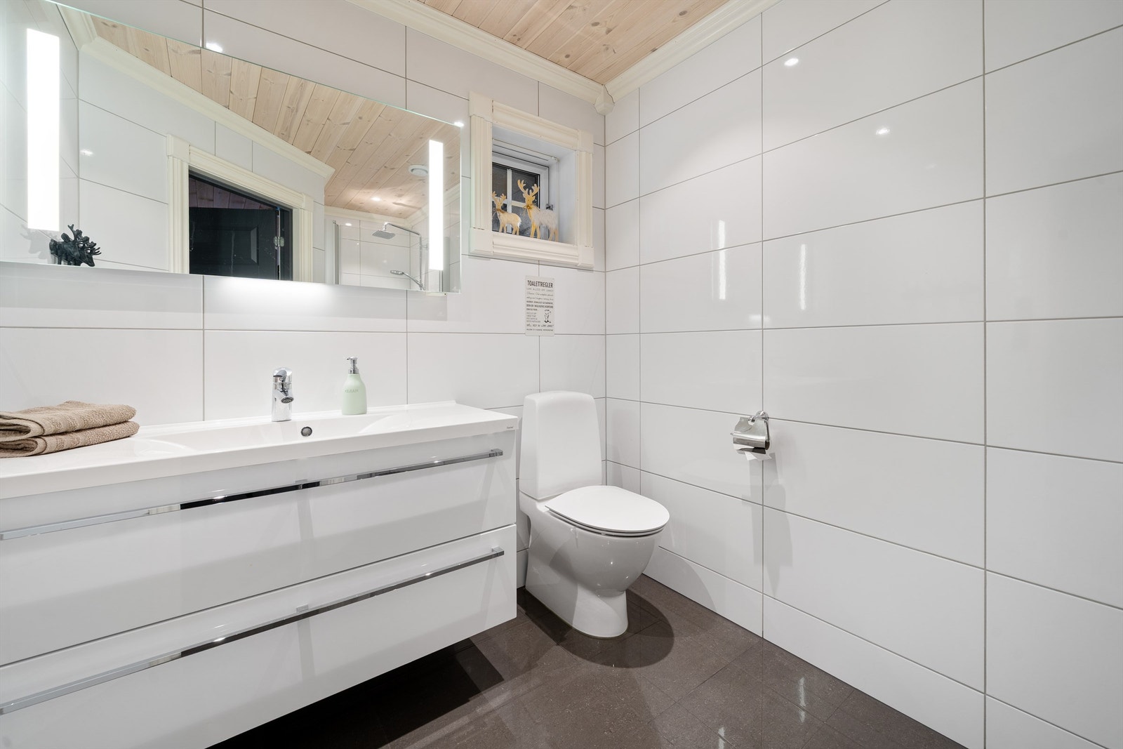 Lyst og innbydende baderom med sor innredning, belyst speil, toalett og dusjnisje. Flislagte gulv og vegger. Galleribilde