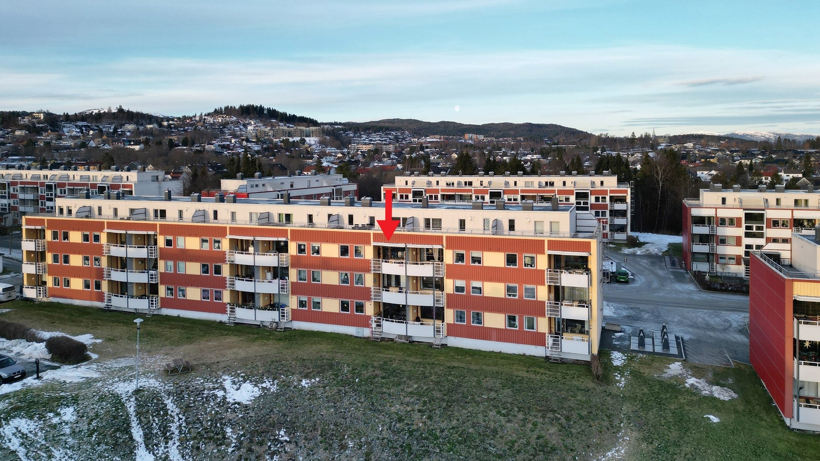 Dronefoto over leiligheten og området rundt. Leilighetens plassering er markert med rød pil. Galleribilde