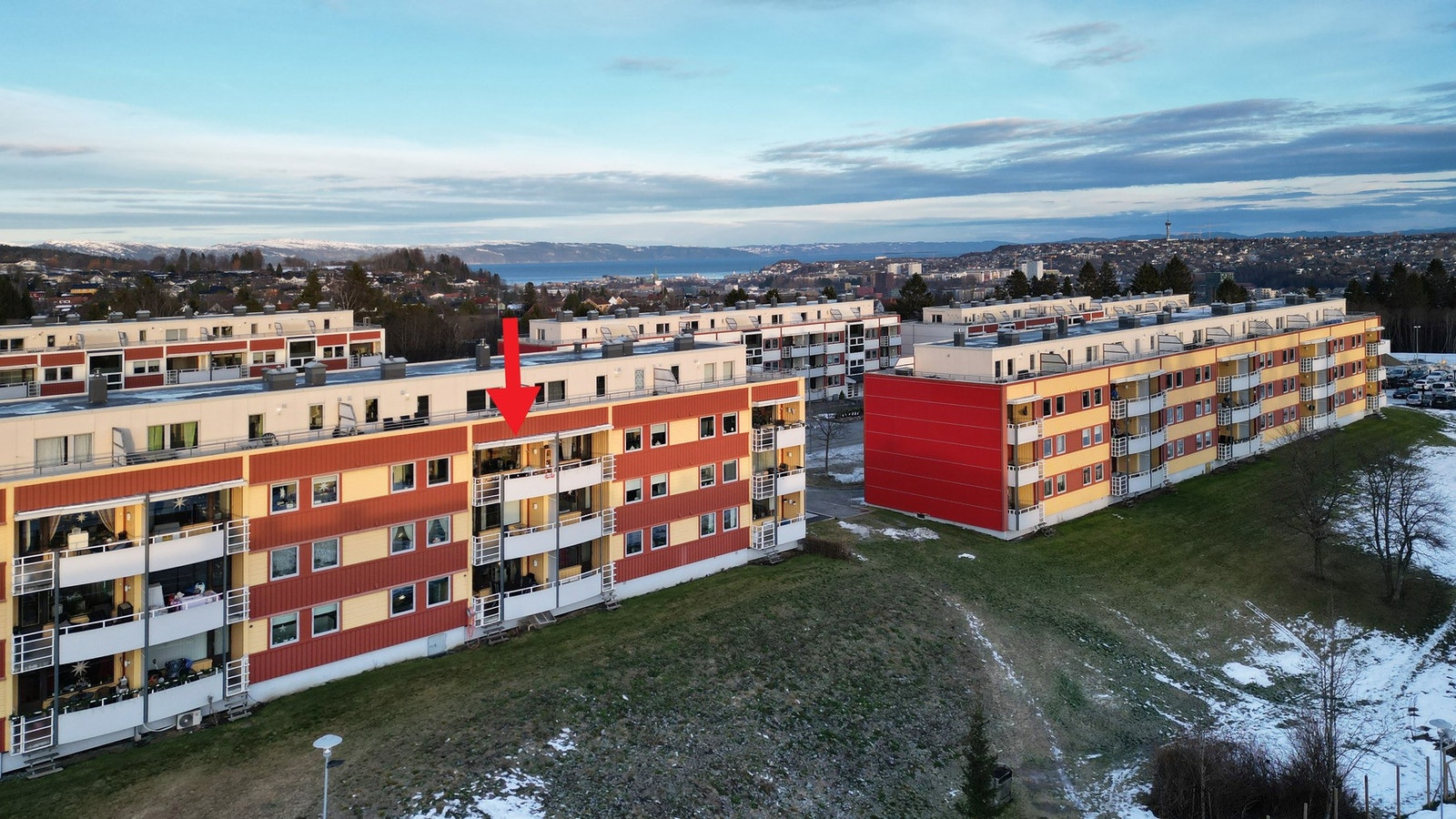 Dronefoto over leiligheten og området rundt. Leilighetens plassering er markert med rød pil. Galleribilde