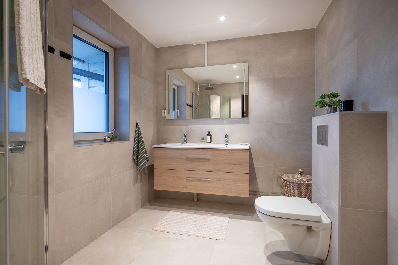 Romslig bad med flislagte flater, innredning med doble servanter og nedsenket dusj med glassdører og toalett. Galleribilde