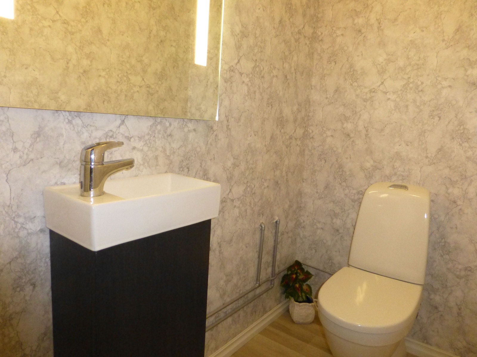 Toalett, oppusset ca 2023. Lyse grå vegger og ekstra lys på speilet. Det er lufteventil på vegg. Galleribilde