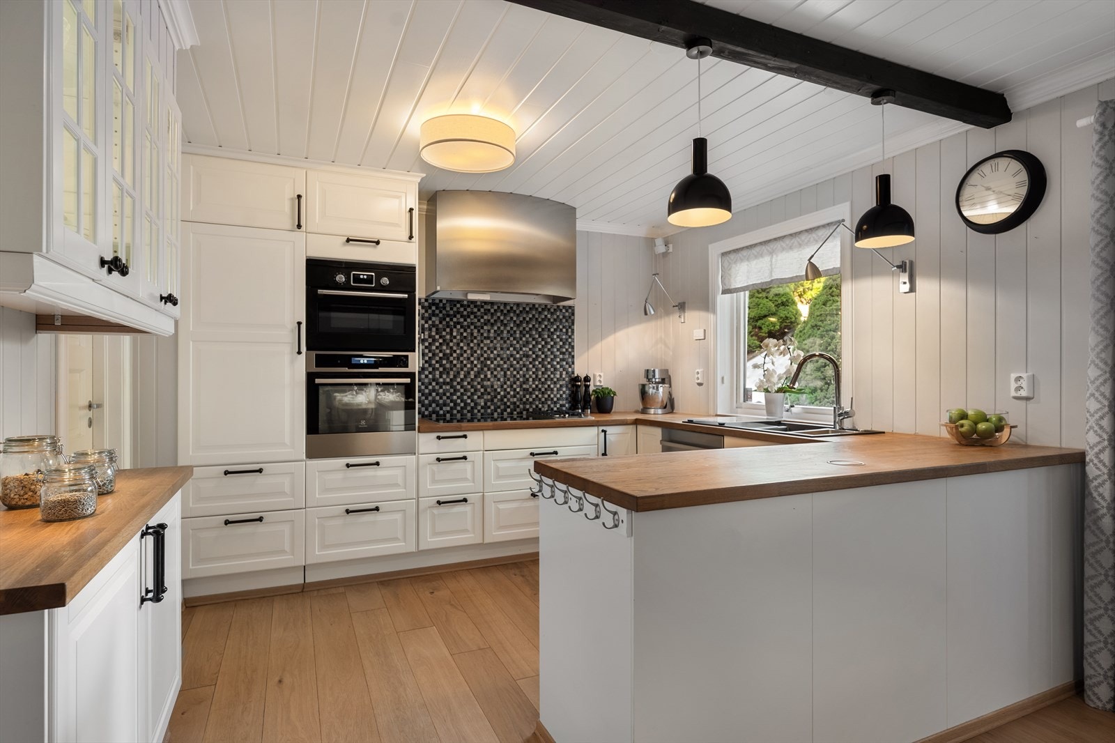 Kjøkkeninnredningen fra IKEA (2013) har hvite, profilerte 1-speils fronter og overskap med glassfronter med sprosser. Benkeplaten i heltre og har nedfelt sort vaskekum i kompositt med ettgreps, krummet blandebatteri. Galleribilde