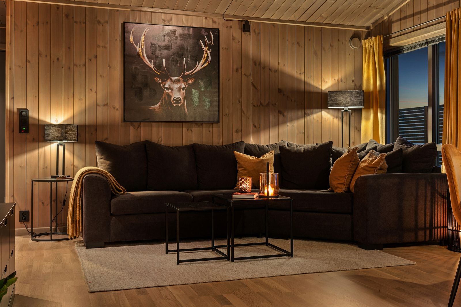 Hytta ønsker deg velkommen inn i en lys og behagelig stue med parkettgulv som gir rommet et elegant og tidløst uttrykk. De lasurbeisede panelkledde veggene tilfører en lun, naturlig stemning og perfekt balanse mellom moderne og klassisk hyttedesign. Galleribilde