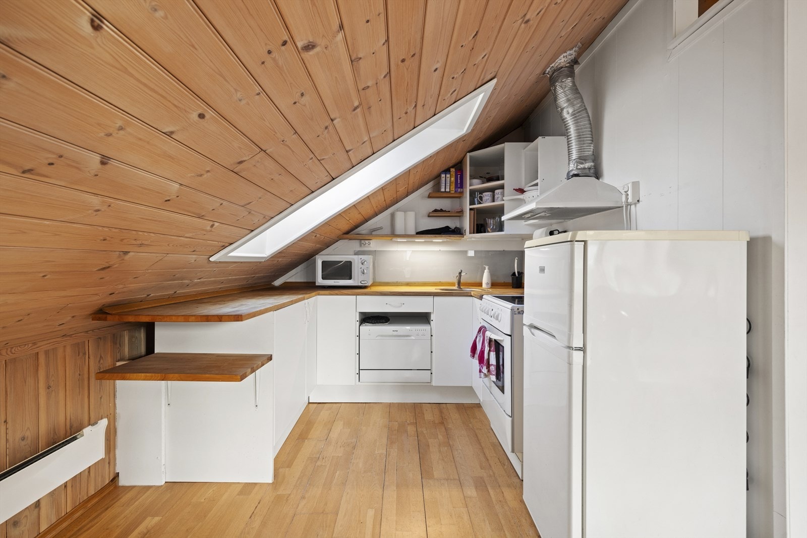 Kjøkkeninnredning med slette fronter og heltre benkeplate. Det er avsatt plass til frittstående kjøl/fryseskap, hybel oppvaskmaskin og komfyr Galleribilde