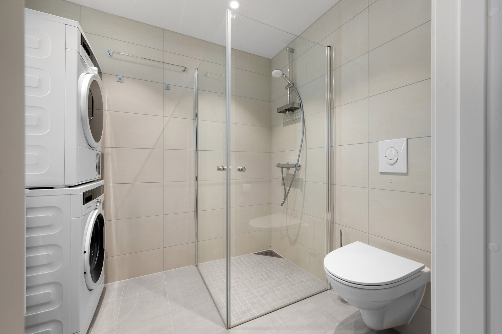 Et stilrent baderom som blant annet er innredet med toalett, dusj, servant med underskap og speil Galleribilde