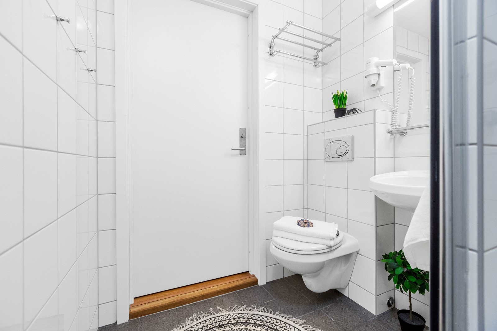 Badene er innredet med hvit porselensservant med ettgreps blandebatteri, vegghengt speil med lyslist over, vegghengt toalett og dusjnisje med glassdør Galleribilde