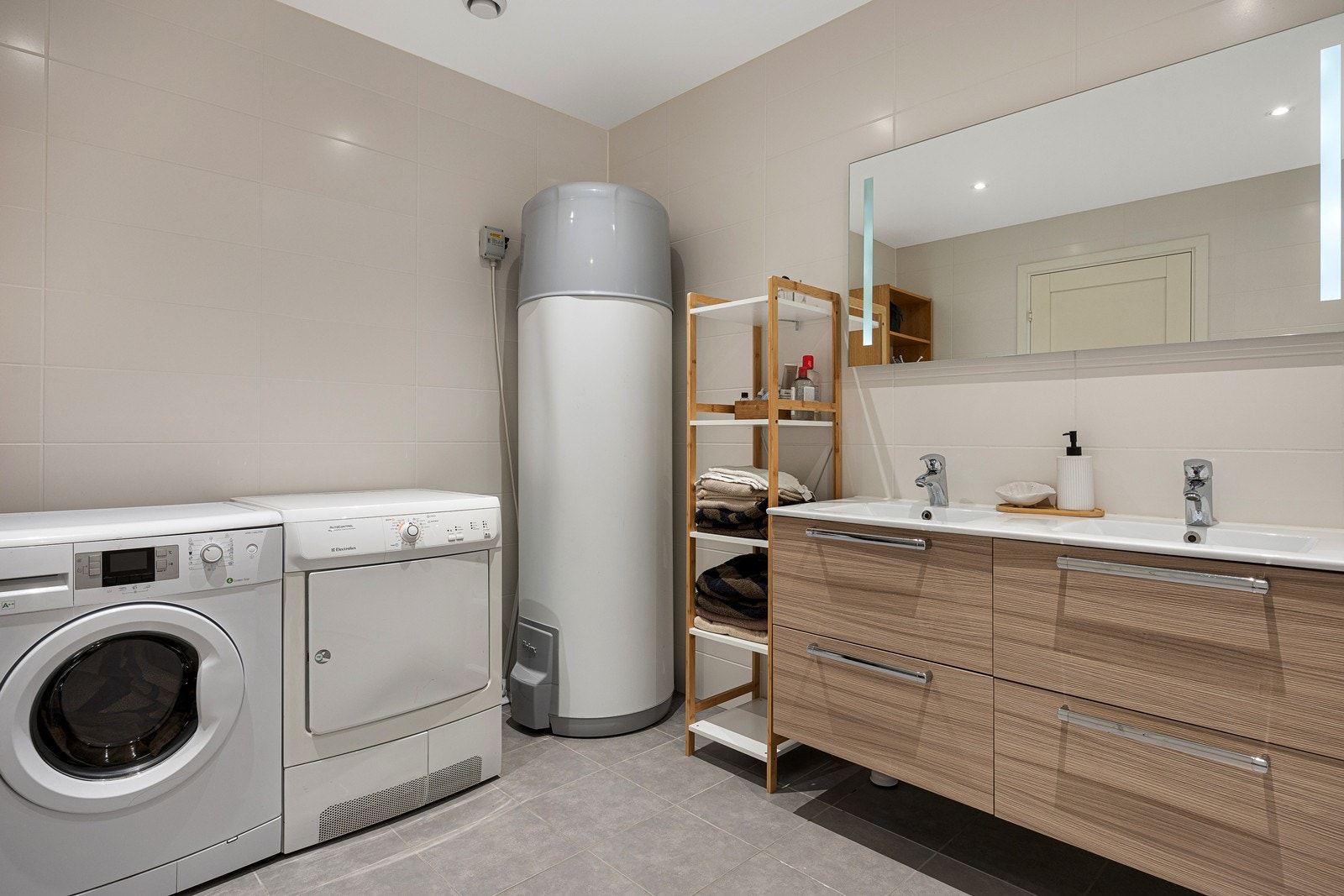 Den øvrige innredningen består av dobbel servant med store skuffer og et stort speil med integrert belysning. Badet har også opplegg for vaskemaskin. Galleribilde