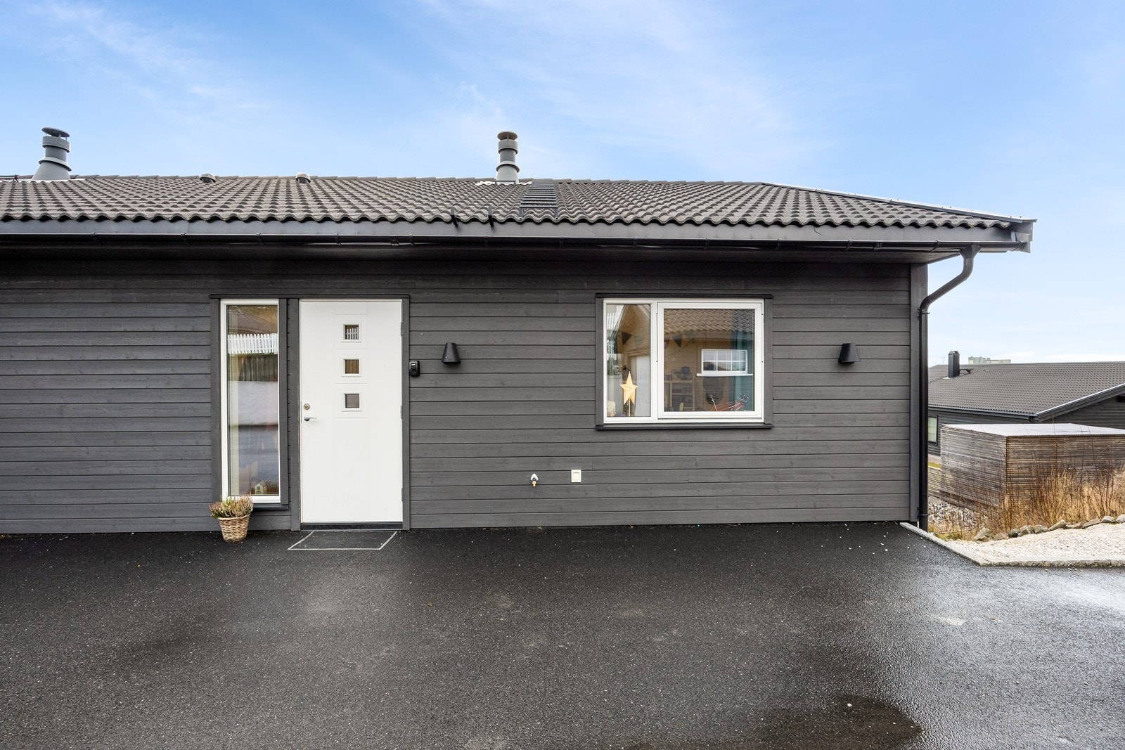 Tomten går over to nivåer, og ved inngangen har boligen en asfaltert gårdsplass for parkering. Gårdsplassen er felles for begge seksjoner. Galleribilde