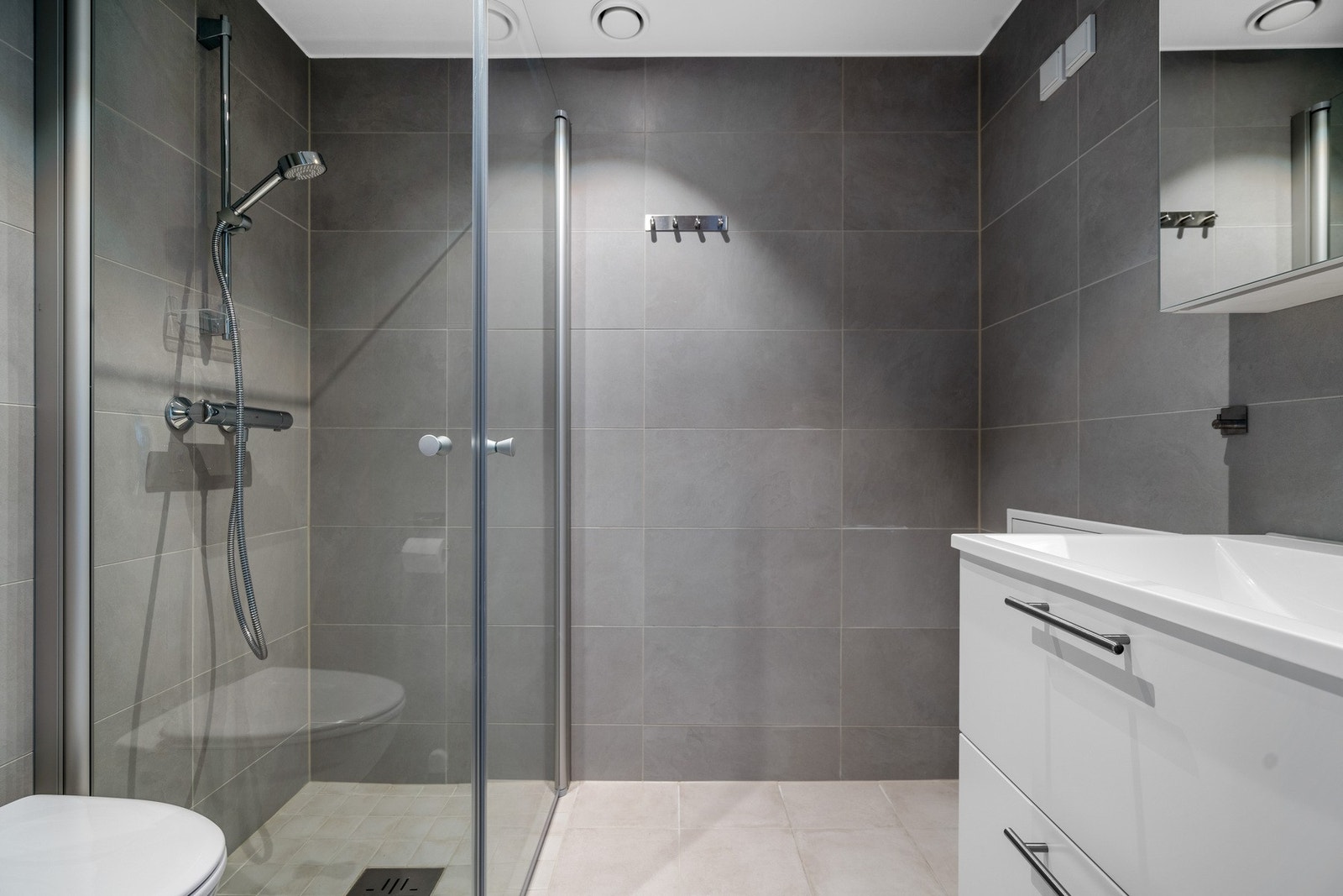 Flislagt bad med vannbåren gulvvarme. Det er innredet med nedfelt servant, veggmontert toalett, dusjvegger/hjørne og opplegg for vaskemaskin. Galleribilde