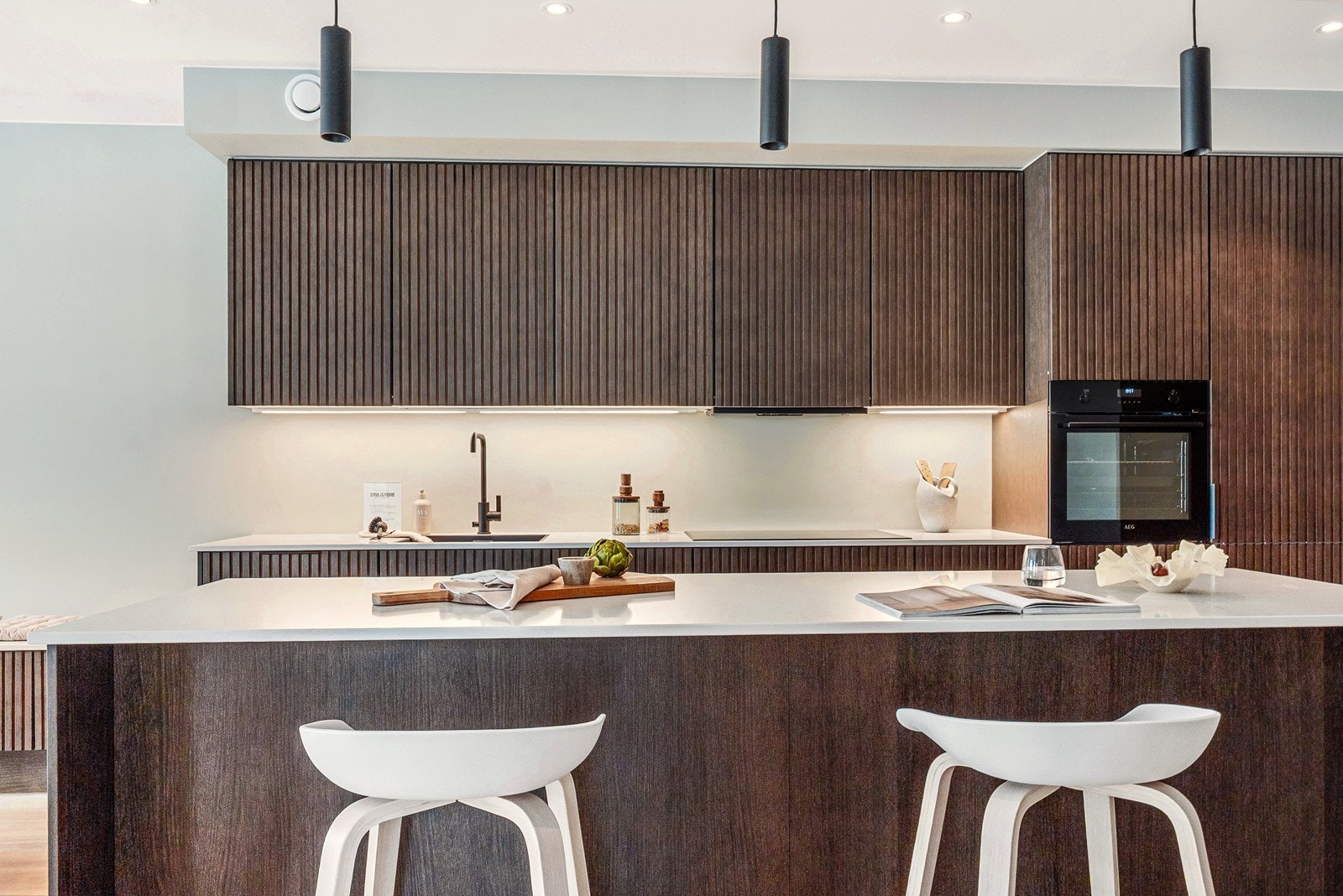 Midt i rommet står et elegant kjøkken fra JKE Design, levert med eikefronter i utførelsen Klassisk Nordic Nature. Kjøkkenøya fungerer som en sosial sone og en praktisk arbeidsstasjon. Galleribilde