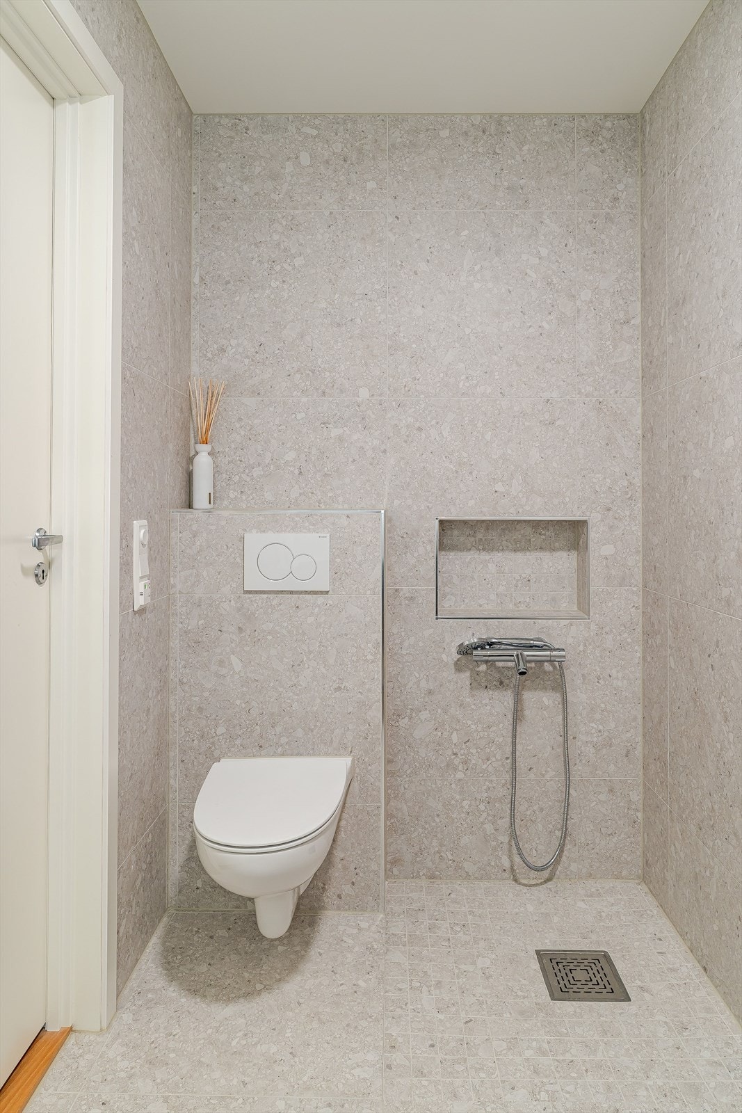 Moderne toalettrom med vegghengt toalett, nisje i vegg og hånddusj, helfliset i delikate, lysegrå fliser. Dette vil kunne være badet i en eventuell hybel/utleiedel. Galleribilde