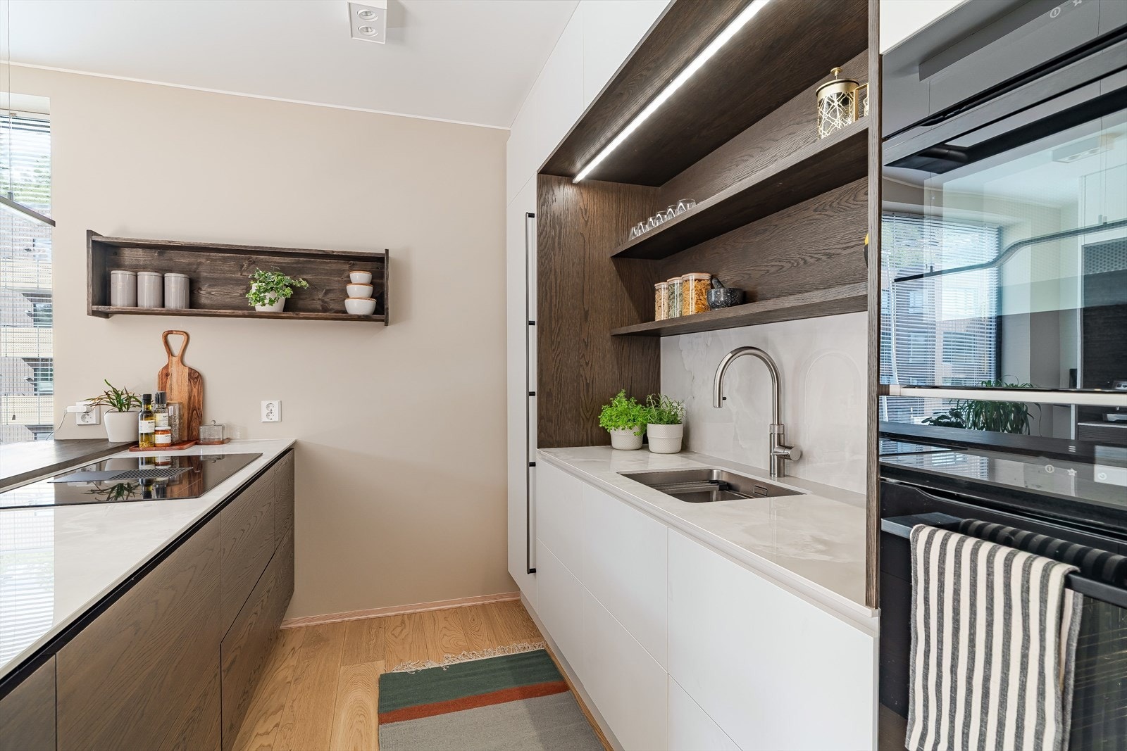 Stilrent kjøkken med integrerte hvitevarer, rikelig med benkeplass og smarte oppbevaringsløsninger. Åpne hyller gir både dekor og funksjon, mens underbelysning skaper en lun stemning. Galleribilde