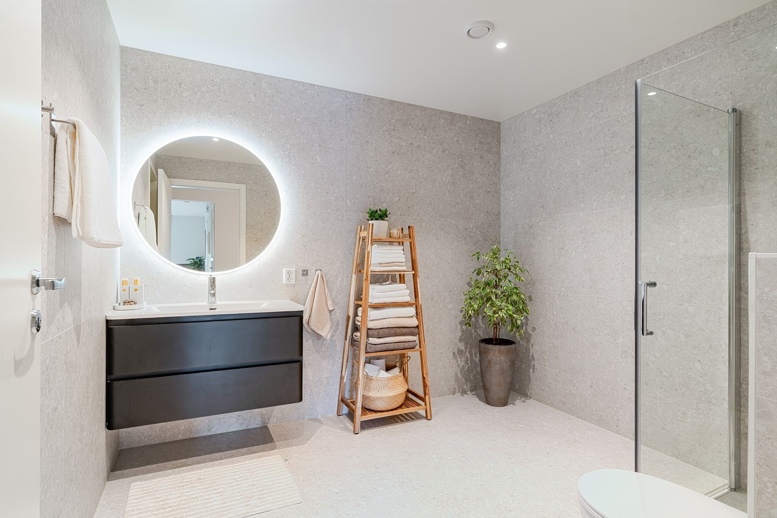 Romslig baderom med store fliser, moderne innredning og rund speil med belysning. Galleribilde