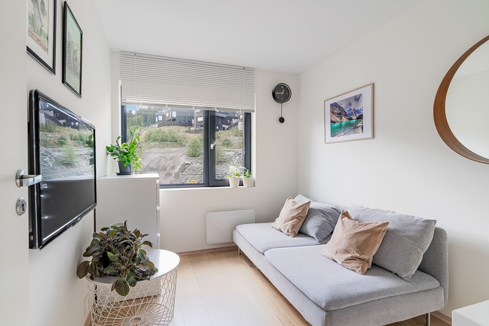 Lyst og hyggelig oppholdsrom innredet med sofa, veggmontert TV og store vinduer som slipper inn rikelig med dagslys. Rommet kan også benyttes som soverom. Galleribilde