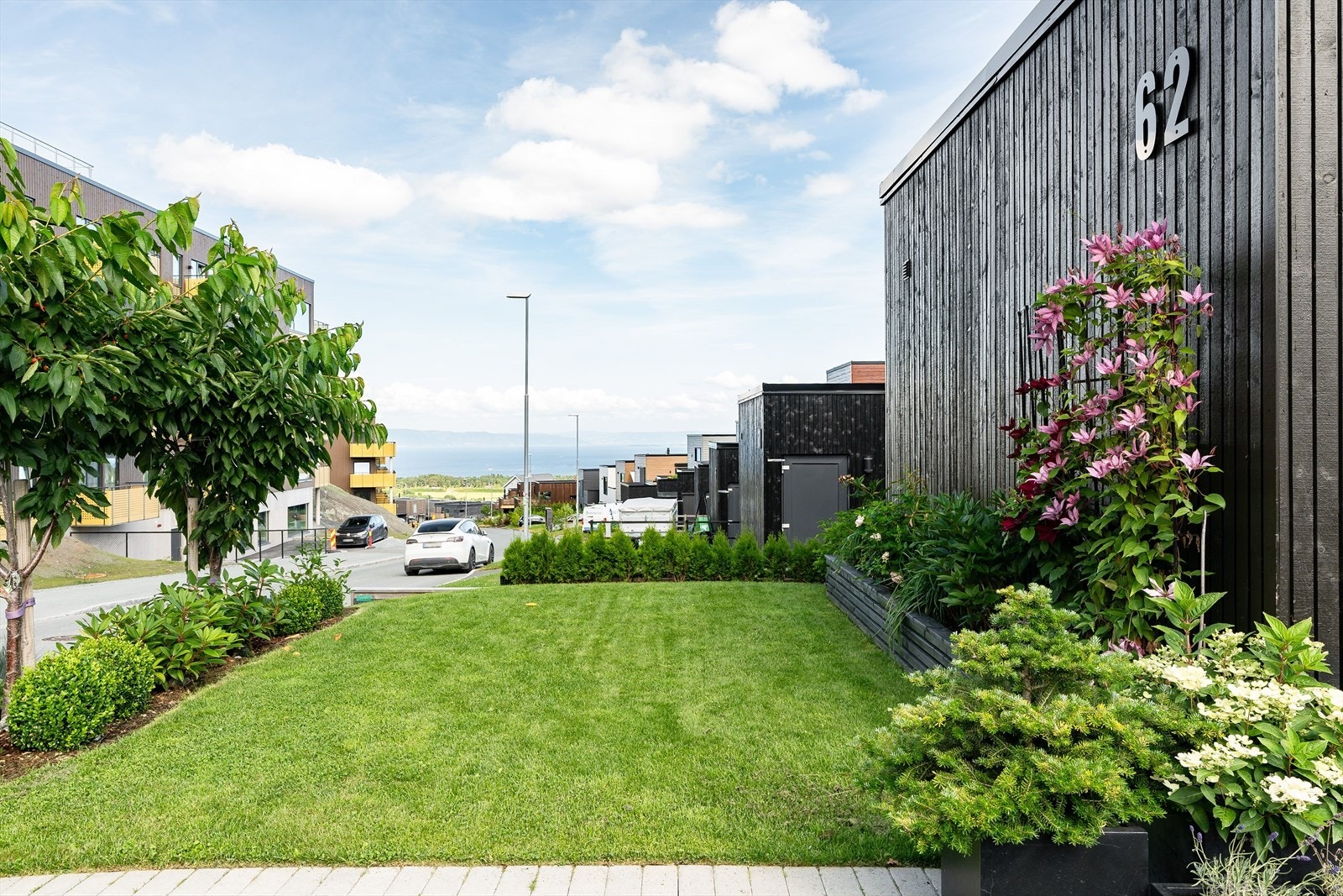 Pent opparbeidet hage med velstelt plen, blomstrende beplantning og innbydende adkomst til boligen. Galleribilde