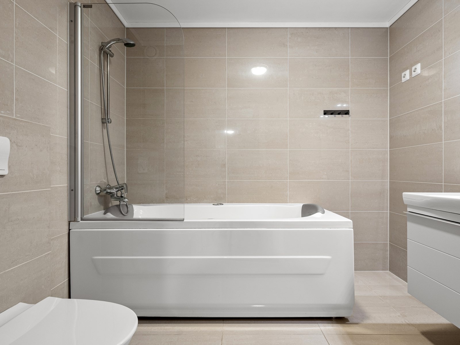 Badet fremstår som et lunt og innbydende rom, utstyrt med et praktisk badekar med innebygd dusj. Denne løsningen gir stor fleksibilitet, enten du ønsker å nyte et langt bad eller ta en rask dusj. Opplegg for maskiner. (Eget vaskerom) Galleribilde