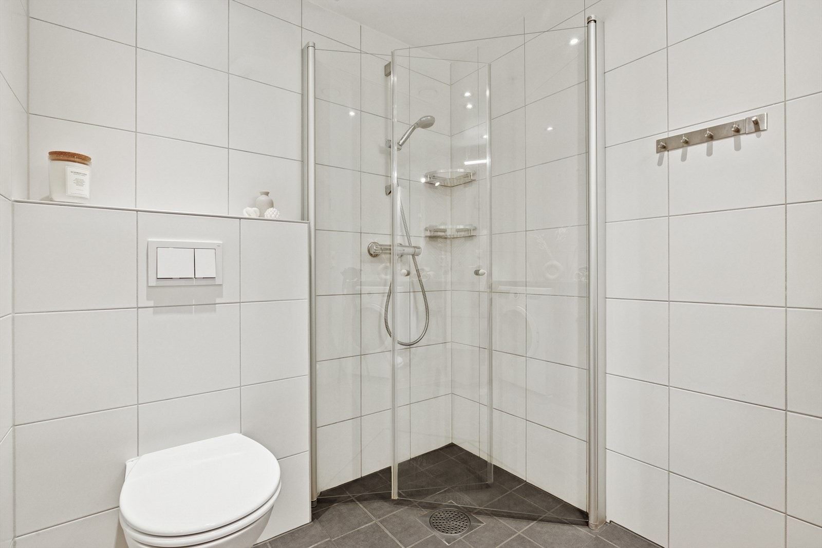 Rommet er innredet med en servant i innredning med ettgreps blandebatteri, veggmontert toalett og en dusjplass med inn- og utadslående dusjvegger. Galleribilde