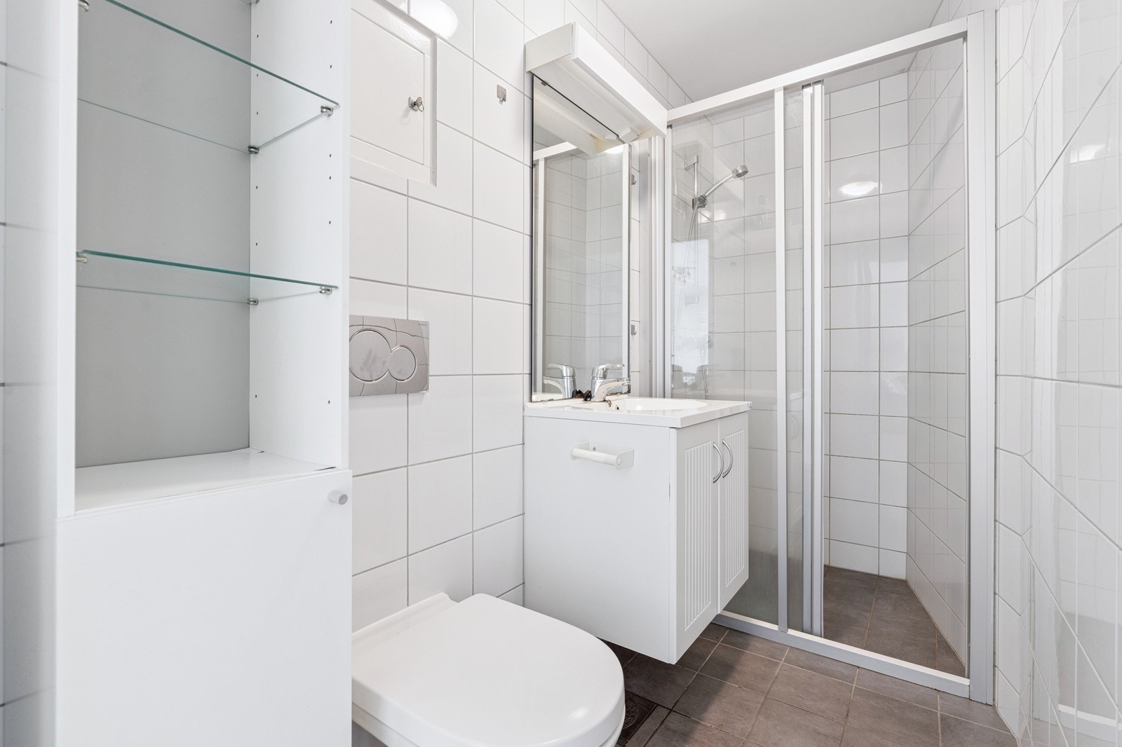 Flislagt med dusjhjørne, servant med underskap, speil og hyller for oppbevaring. Galleribilde