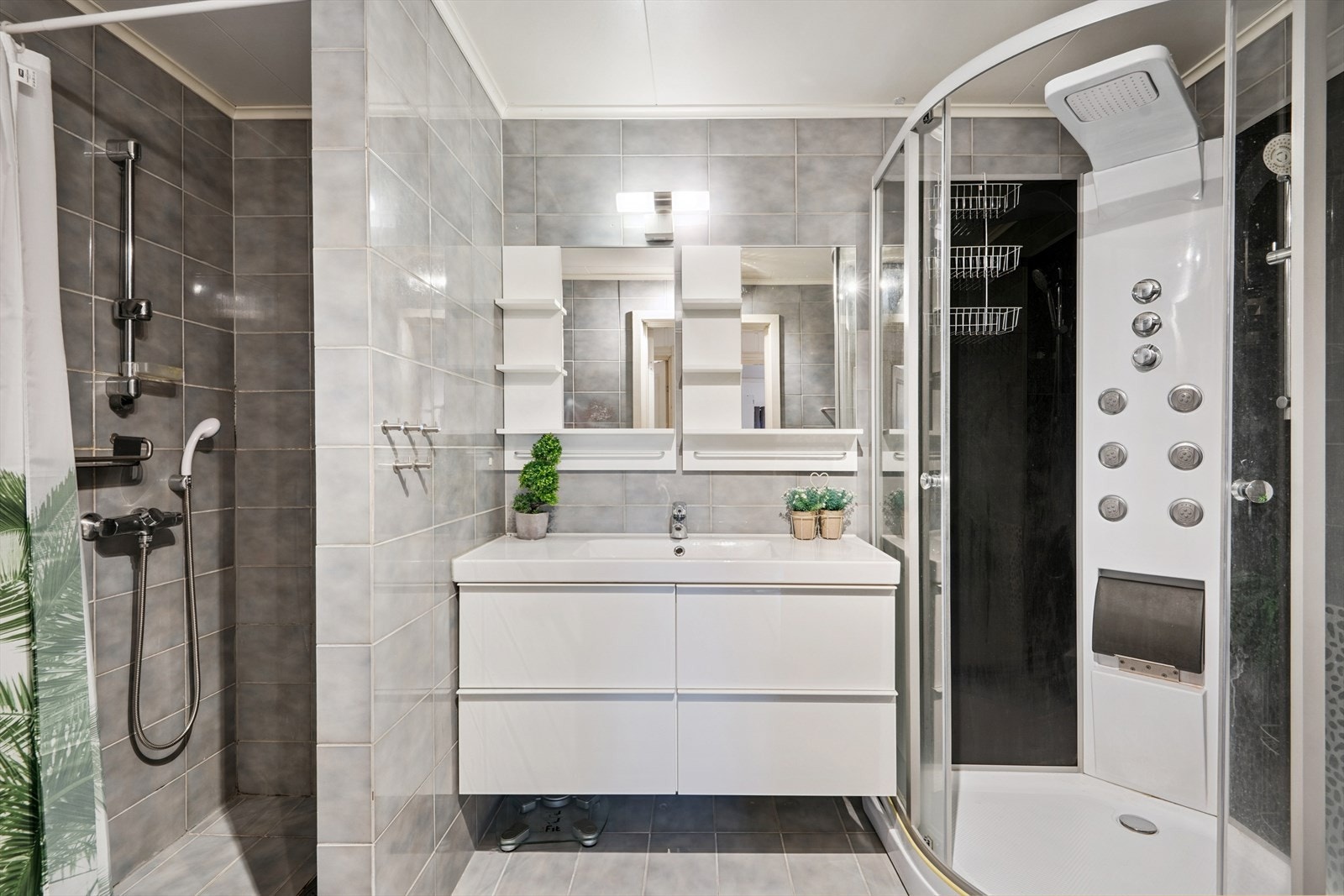 Badet er romslig, med grå fliser på gulv og vegger. Det var tidligere badekar der dusjkabinettet i dag står, men dette ble fjernet for noe år siden. Så her kan flere dusje på en gang om man ønsker dette. Galleribilde