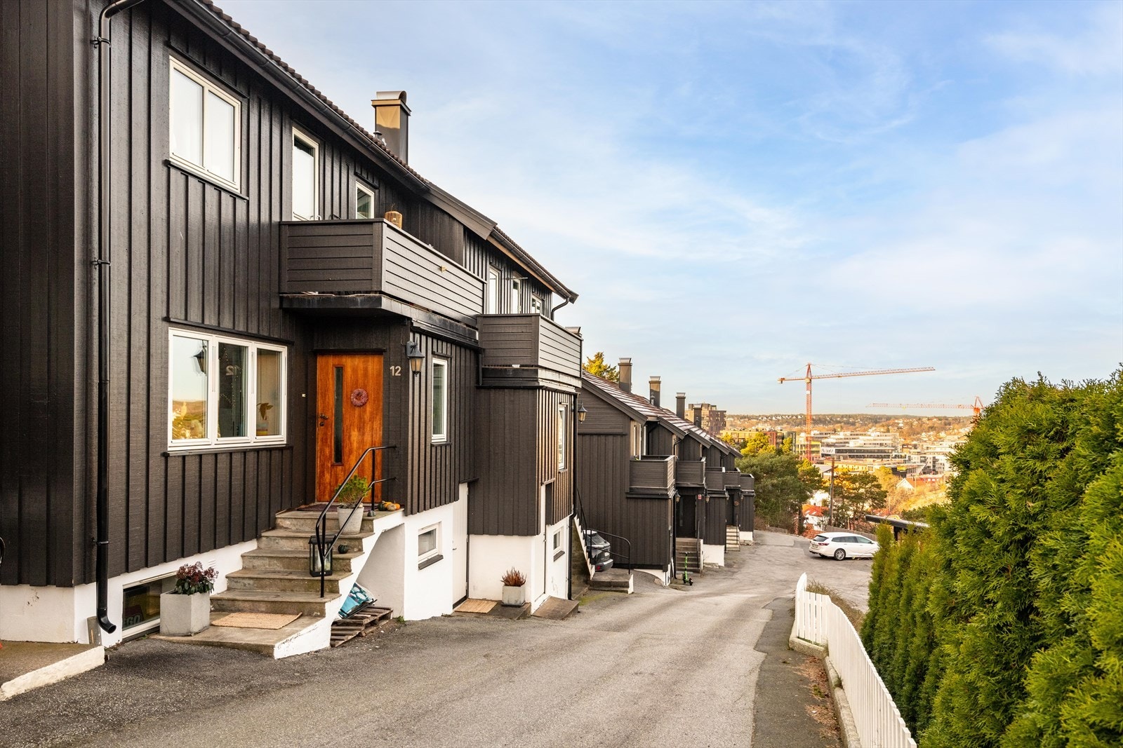 Inngang til boligen opp en liten trapp, og inngang til kjelleren i underetasjen. Parkeringsplass med lader 20 mellom bygningene på bildet Galleribilde