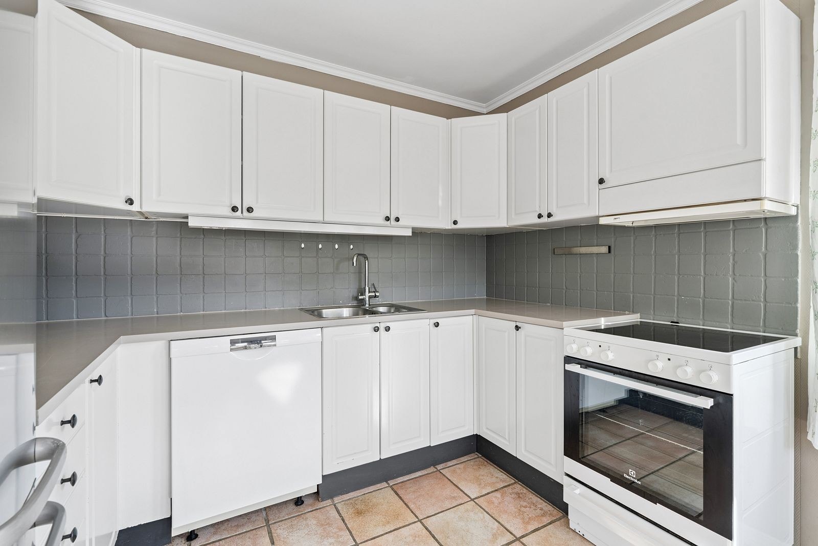 Kjøkken med hvite fronter og frittstående komfyr, oppvaskmaskin og kjøleskap. Galleribilde