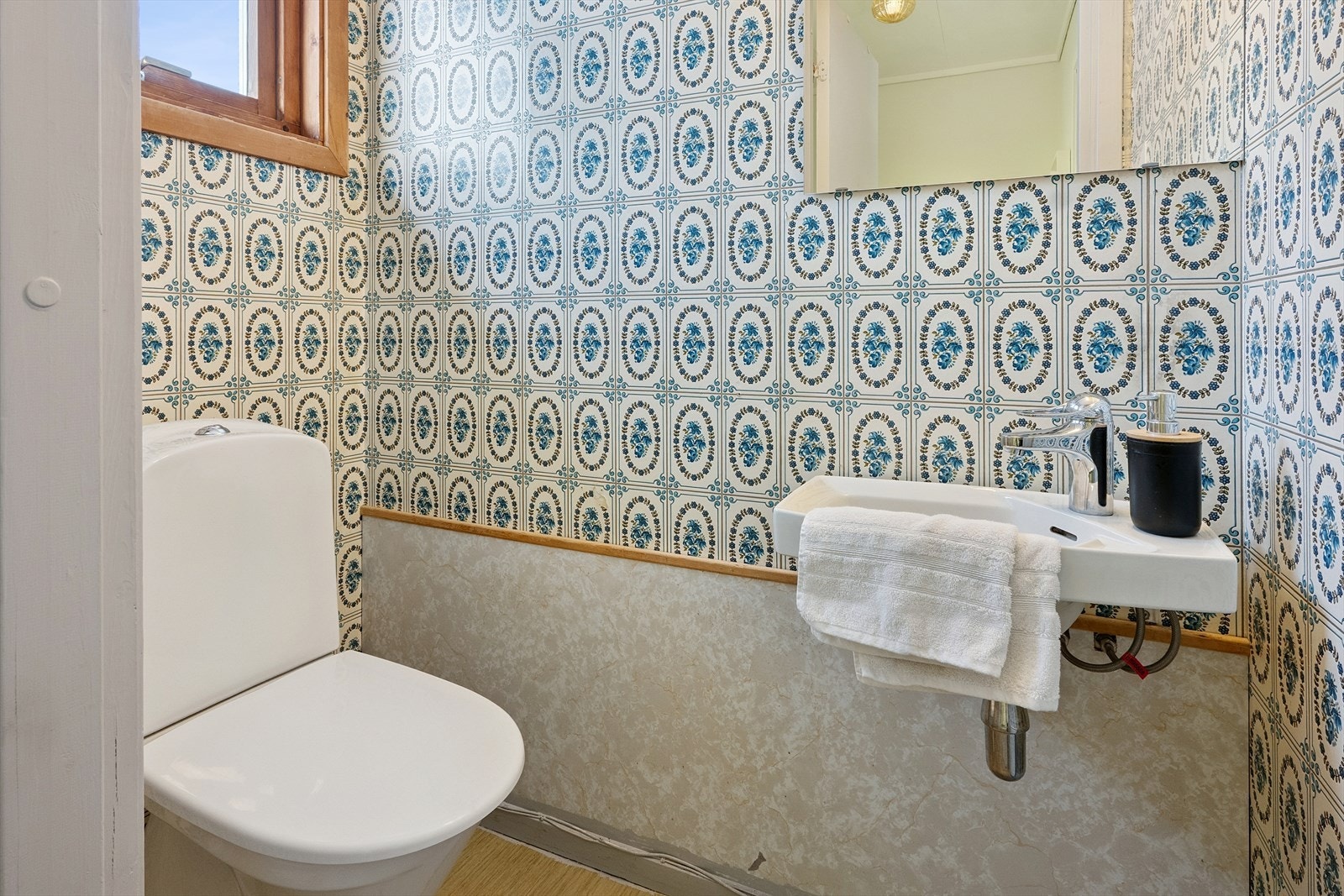 Praktisk toalettrom med belegg på gulv, tapet og en type respatexplater på nedre del på vegg mot baderom og malte plater i tak. Galleribilde