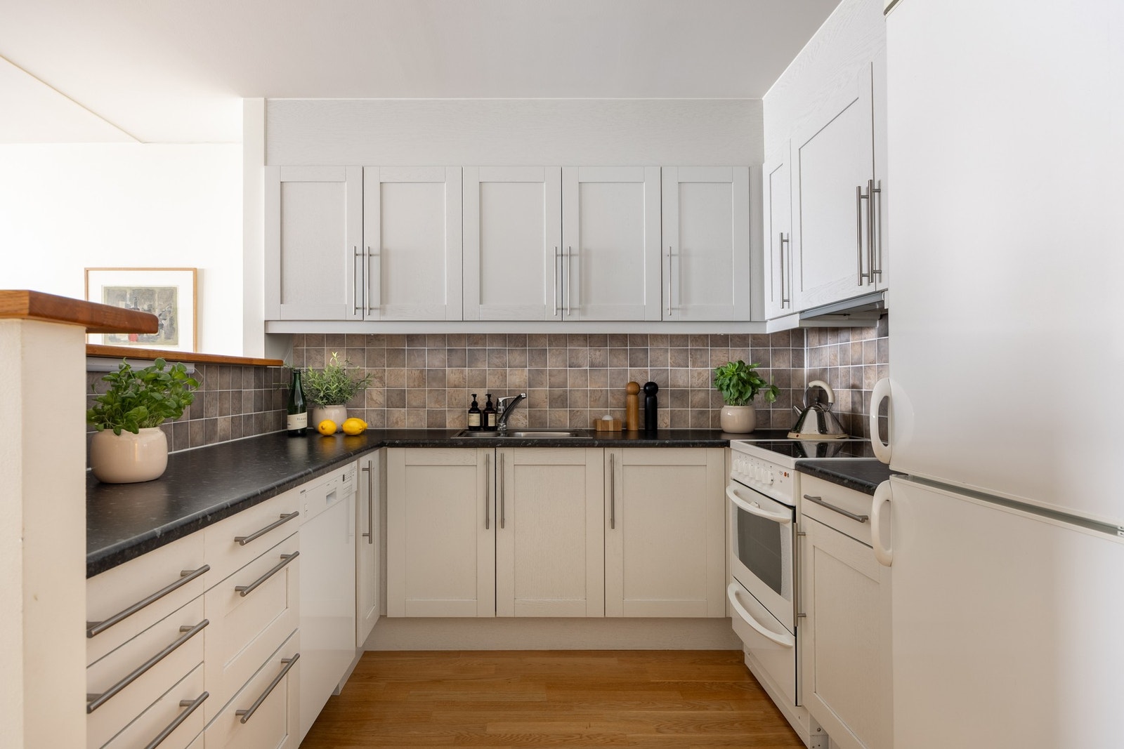 Tidløs kjøkkeninnredning med hvite finérte fyllingsfronter og benkeplate i laminat Galleribilde