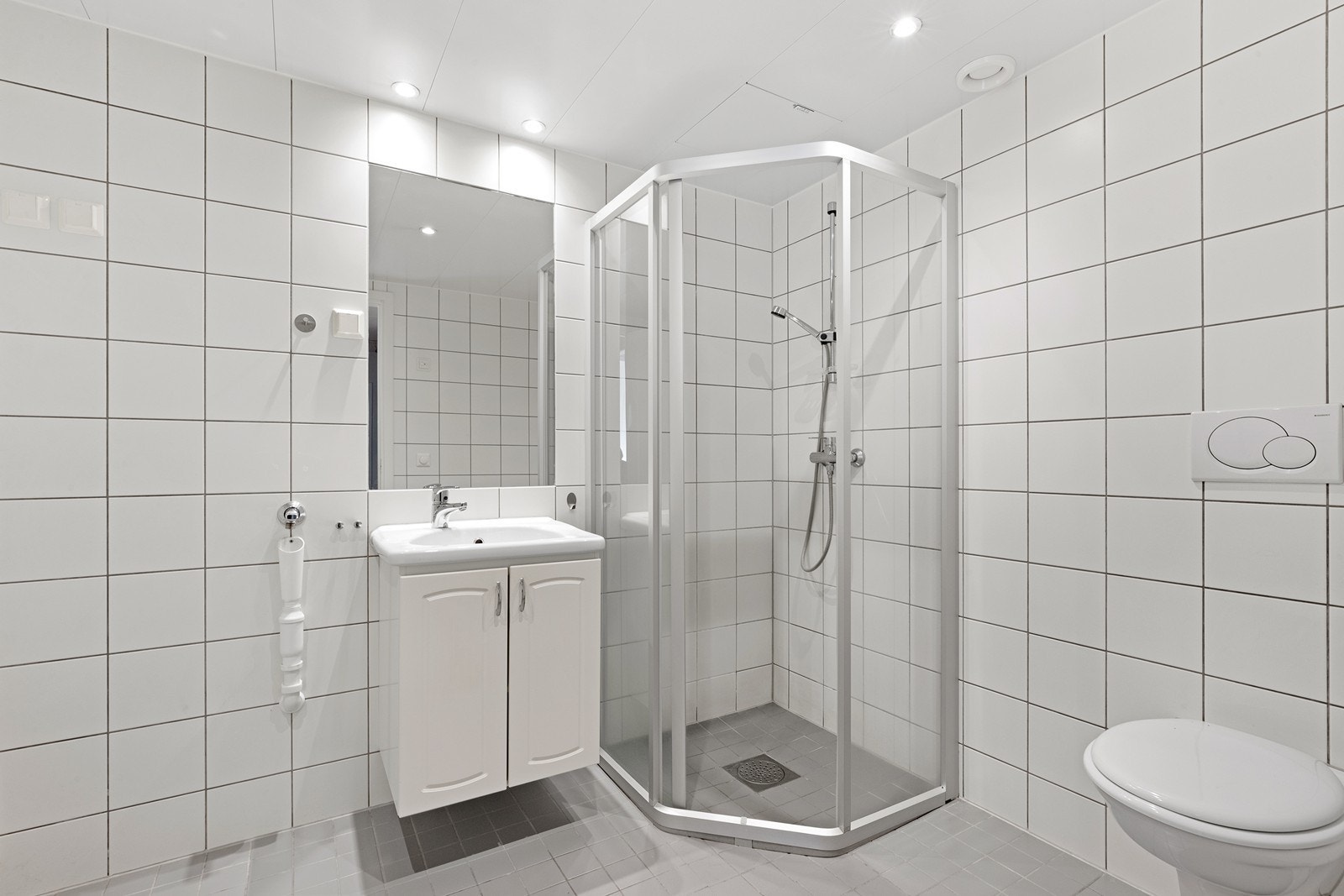 Et pent, flislagt bad med dusjhjørne, servantinnredning og opplegg for vaskemaskin. Galleribilde