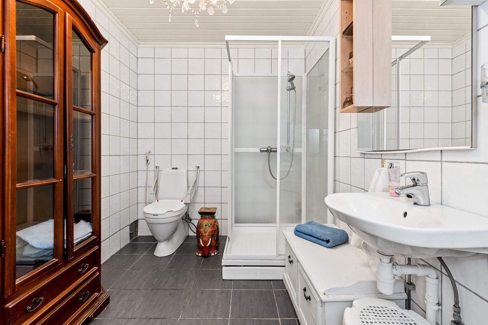 Flislagt bad innredet med dusjkabinett, en enkel servant med overhengende speil, samt toalett. Galleribilde