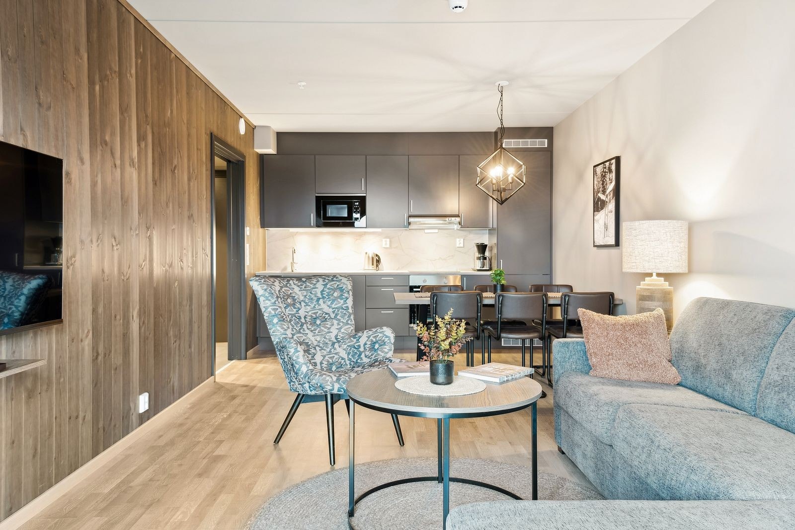 Som en kontrast til de ellers lyse overflatene med 3-stavs parkettgulv og lysmalte veggflater og himling er en stuevegg kledd med panel i lun fargetone. Galleribilde