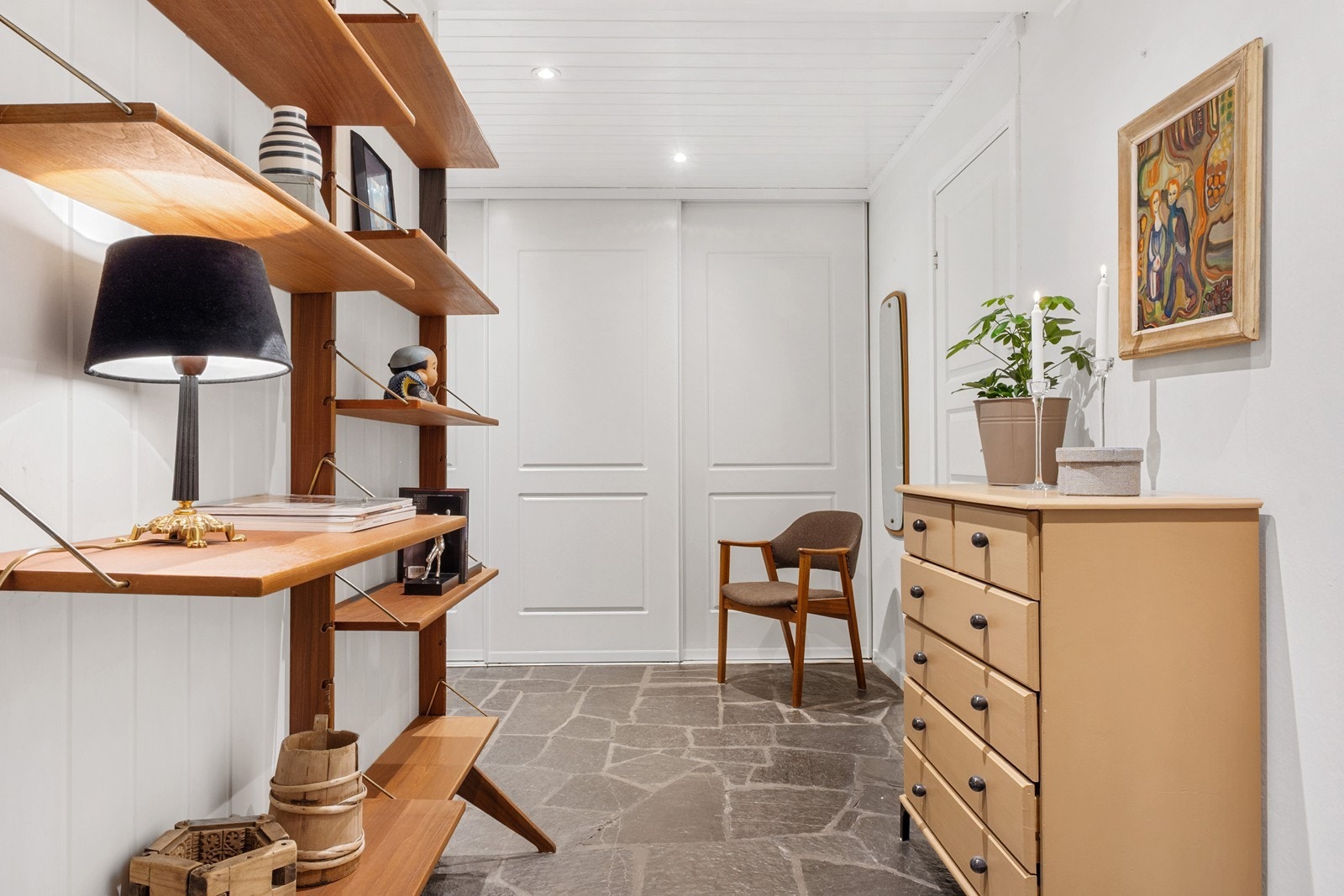 Gangen har en gjennomført stil med flislagt gulv i skifer og downlights i himlingen. Rommet oppleves luftig og funksjonelt, med god plass til garderobeløsning i form av en praktisk skyvedørsgarderobe. Galleribilde