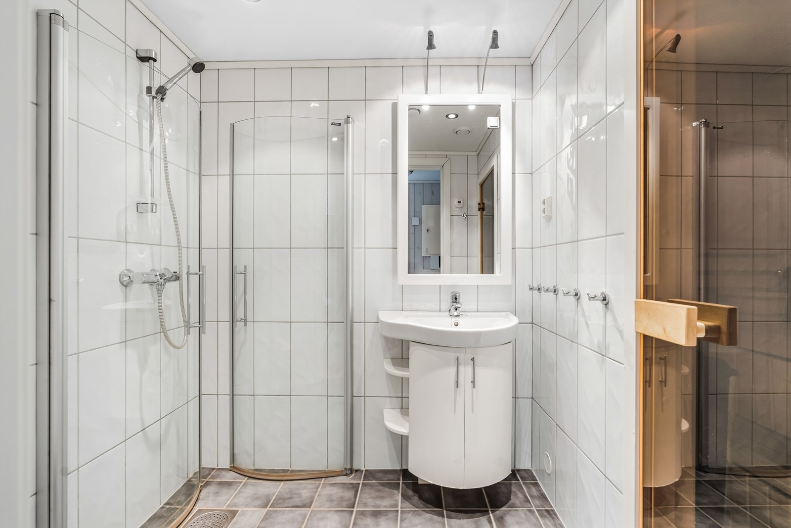 Badet er helfliset på gulv og vegger, og innredet med dusjvegger, vegghengt toalett og servant med speil. Galleribilde