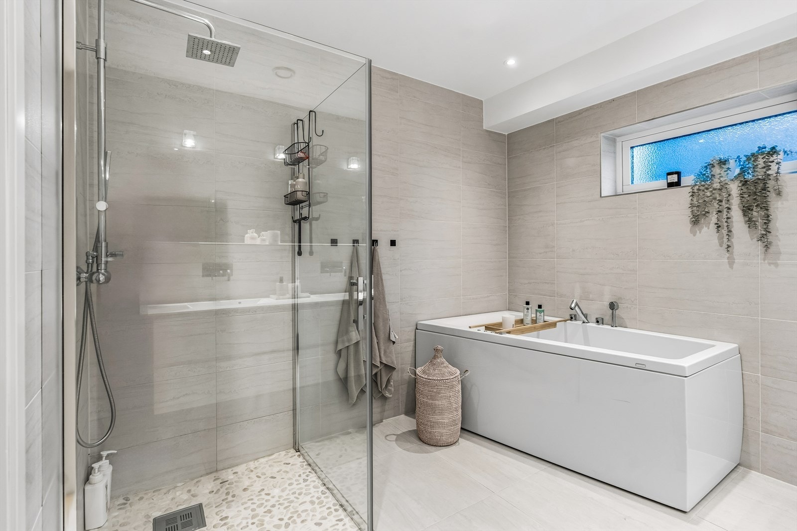 Badet har badekar og dusjhjørne med glassdører. De flislagte veggene har brede fliser i en behagelig sandtone, og gulvflisene er store og lyse. Galleribilde