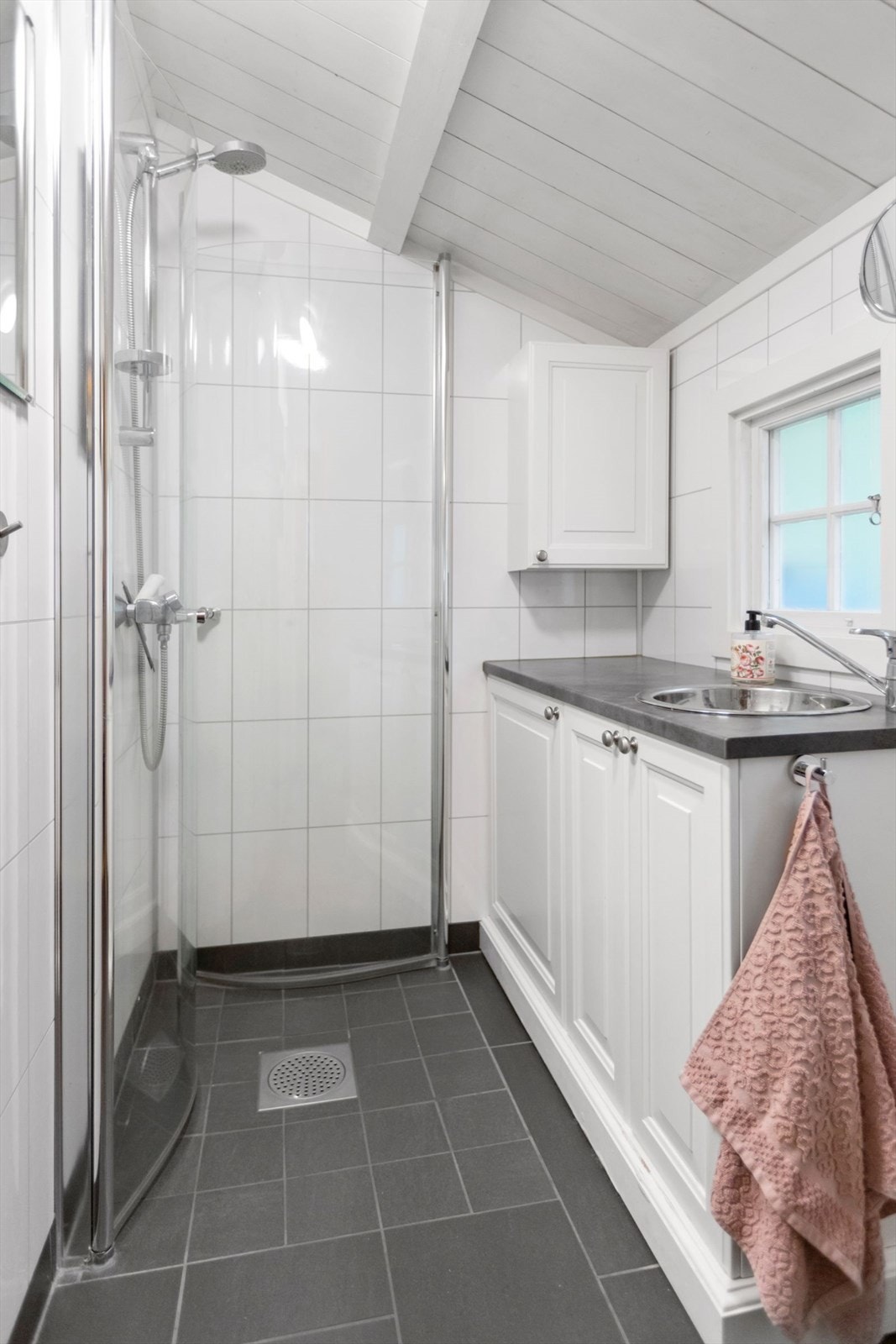 Bad med flislagt gulv med varmekabler, baderomsplater på vegger og panel i tak. Innredning med servant. Dusjhjørne med foldbare vegger og vegghengt dusjarmatur. Galleribilde