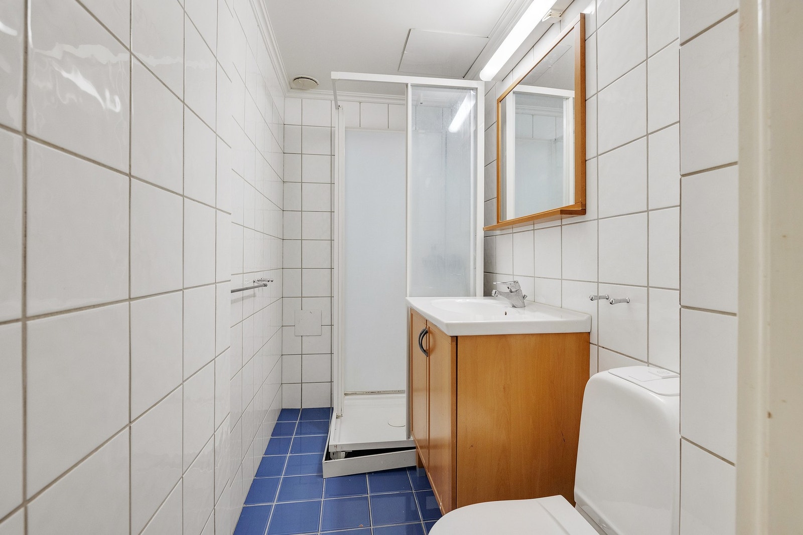 Flislagt bad med servantskap, dusjkabinett, speil og lysarmatur med stikkontakt. Galleribilde