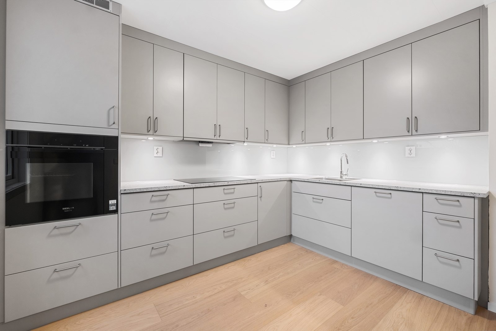 Det er glatte fronter, benkeplate med nedfelt stålvask og glassplate på vegg over benk - Legg også merke til den gode belysningen med downlights under overskapene Galleribilde