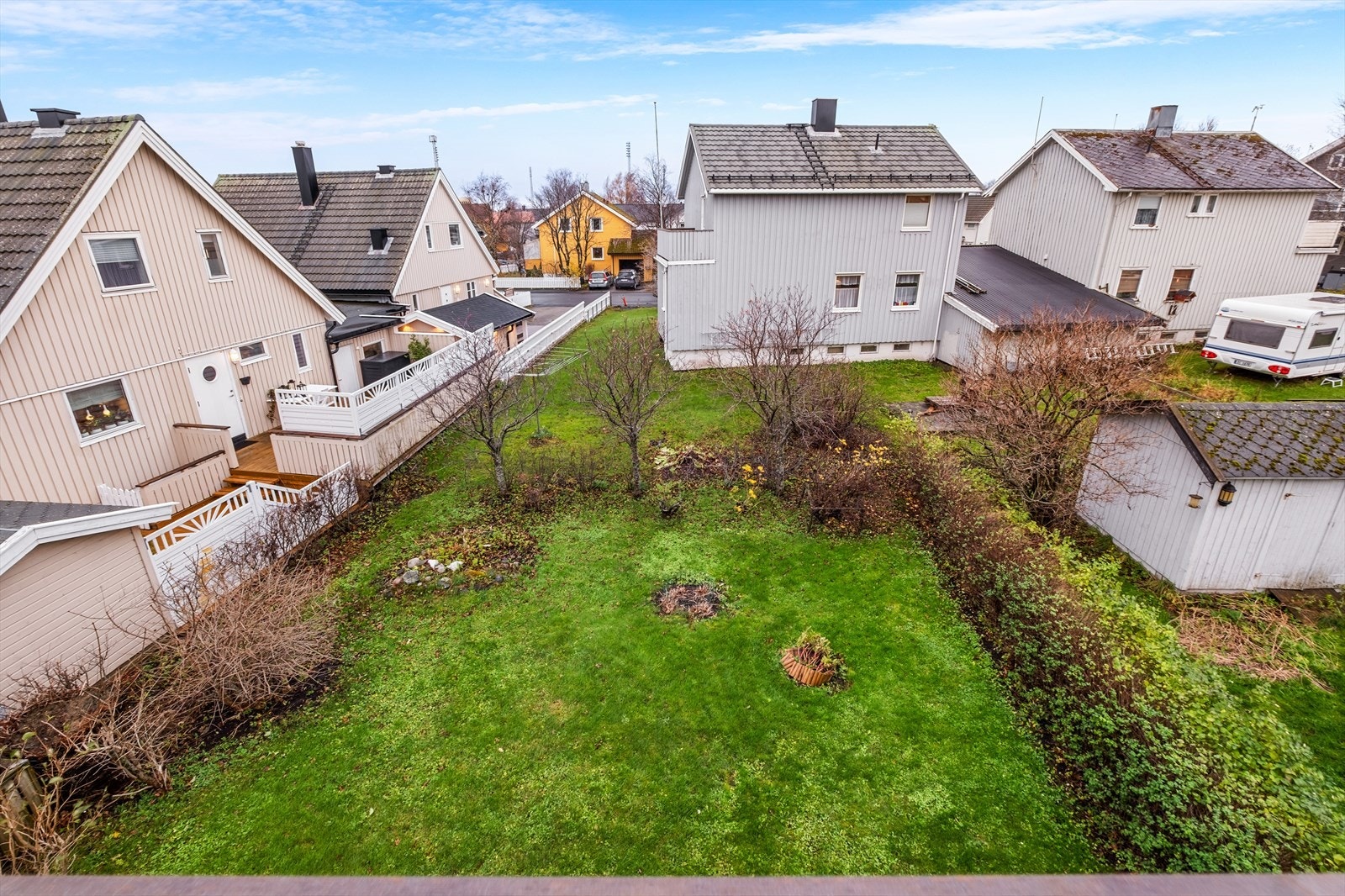 Det er utgang fra stuen i 1. etasje til en pent opparbeidet hage med plen og diverse beplantning Galleribilde