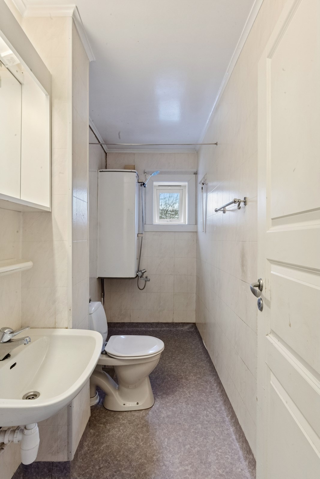 Badet er av eldre dato og er innredet med grått gulvbelegg og baderomstapet på vegg. Galleribilde