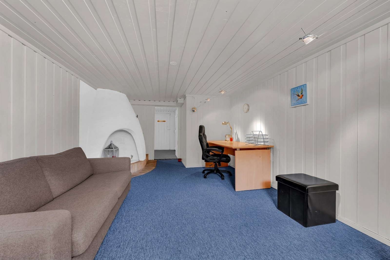 Kjellerstue med tepper og malte trepanel på vegger og tak. Galleribilde