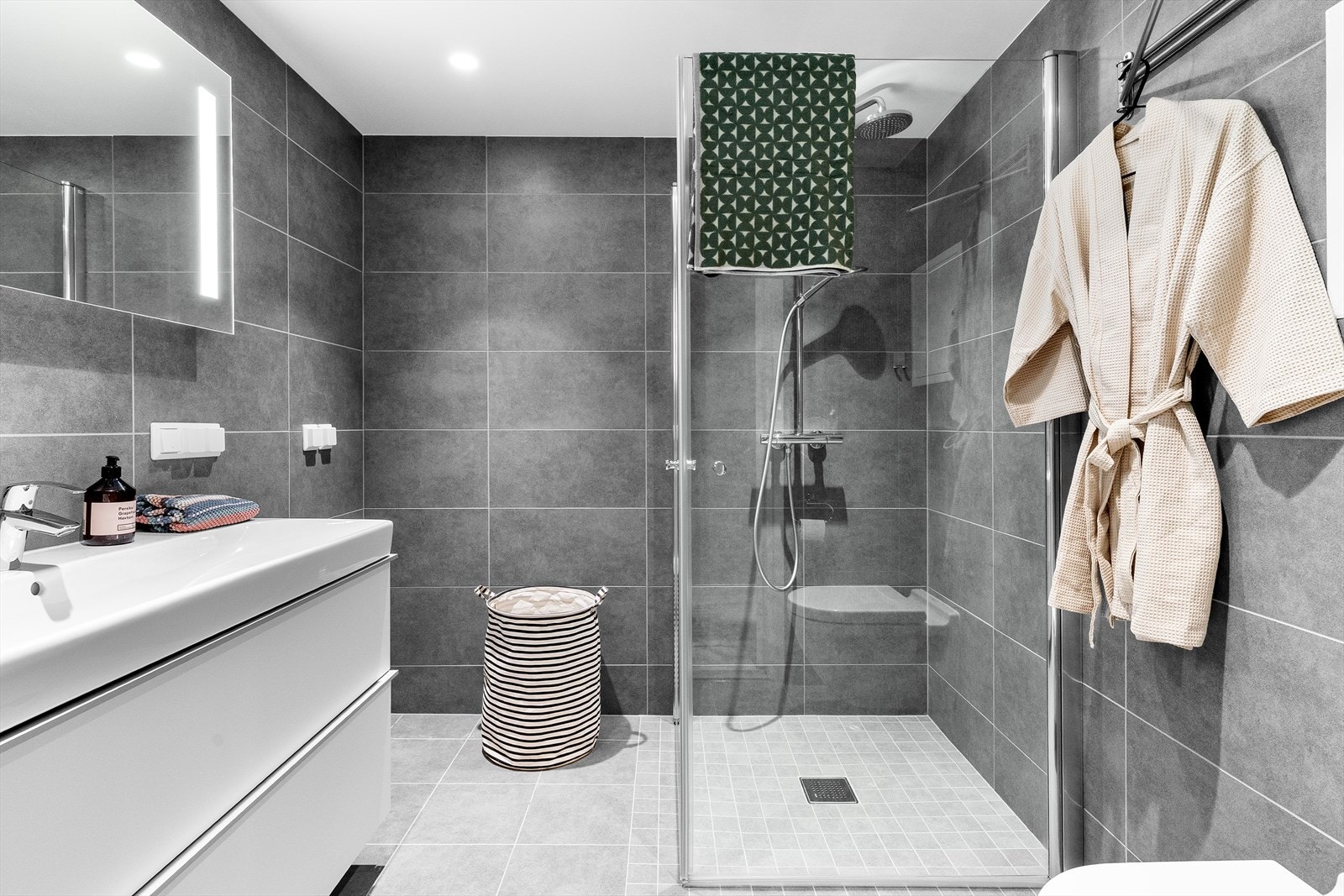 Stilrent og moderne bad med mørke fliser, varmekabler i gulv og en utstrakt bruk av downlights i himling. Galleribilde