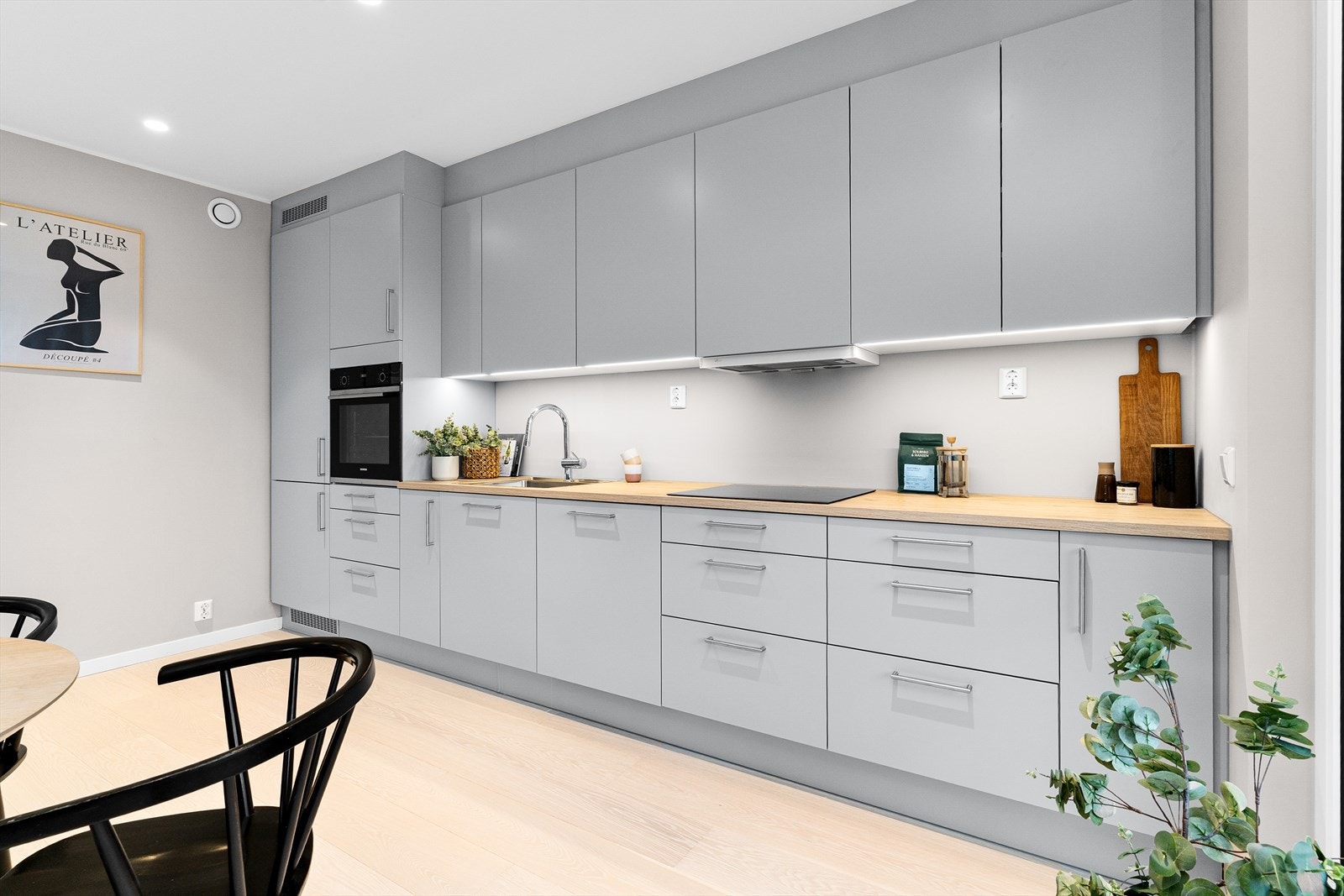 De slette overflatene og den gjennomførte belysningen under overskapene fremhever kjøkkenets moderne estetikk. Galleribilde