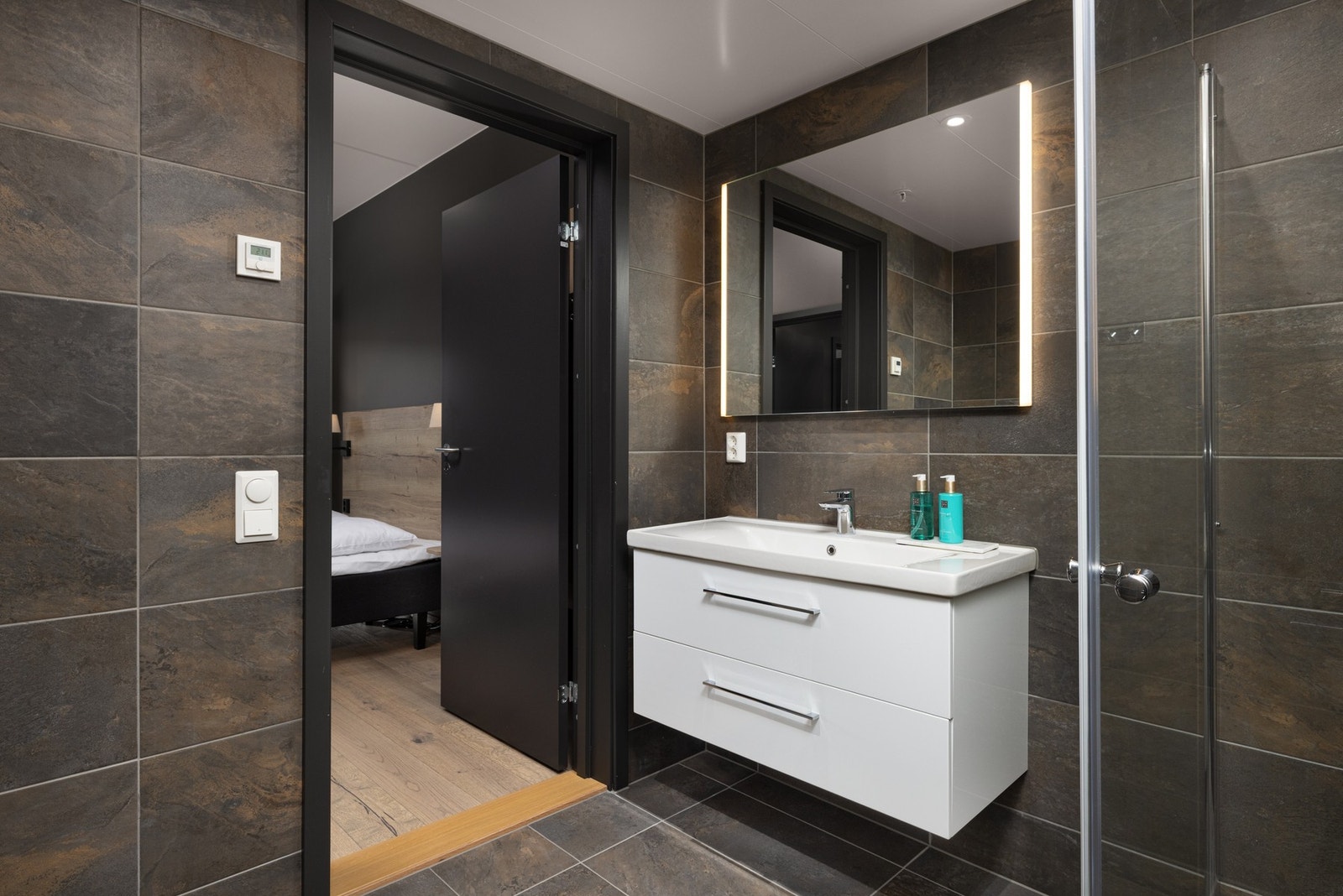 Rommet er innredet med nedfelt servant, veggmontert toalett, dusjhjørne med innfellbare dører samt opplegg for vaskemaskin. Galleribilde