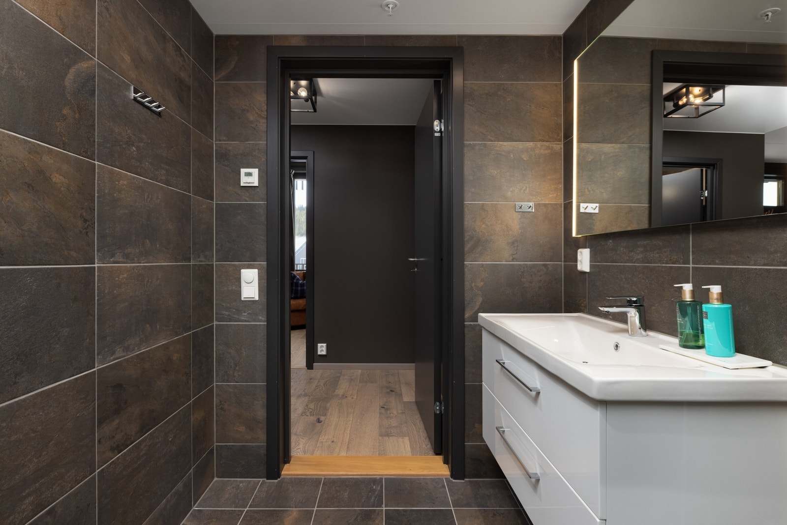 Badet har inndredning med nedfelt servant med underskuff, speil, veggmontert toalett og dusjhjørne med innfellbare glassdører. Galleribilde