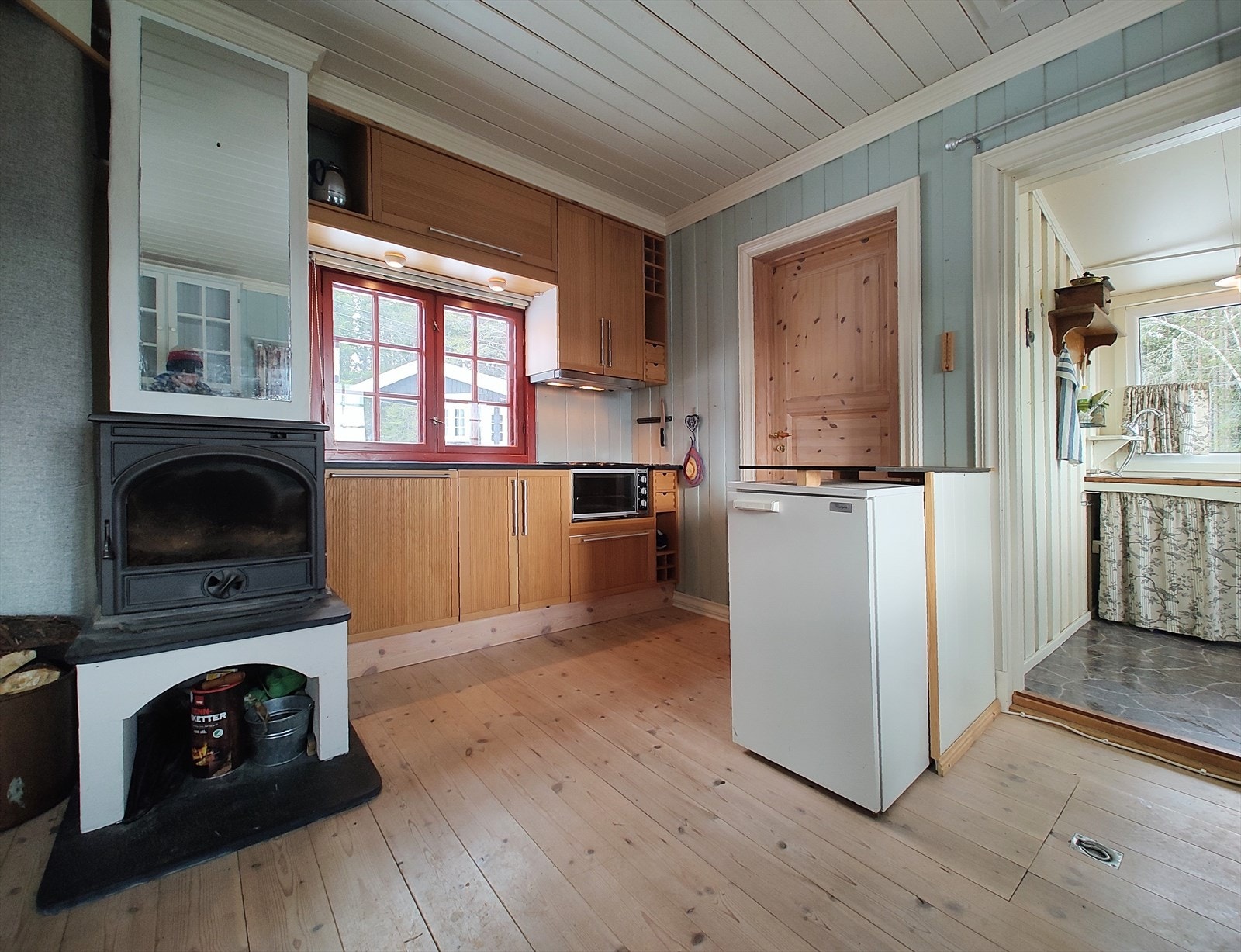 Enkel kjøkkeninnredning med skrog og profilerte skapdører i laminat, med benkeskap og overskap. Benkeplate er av stein. Hybelkomfyr og et lite kjøleskap. Galleribilde