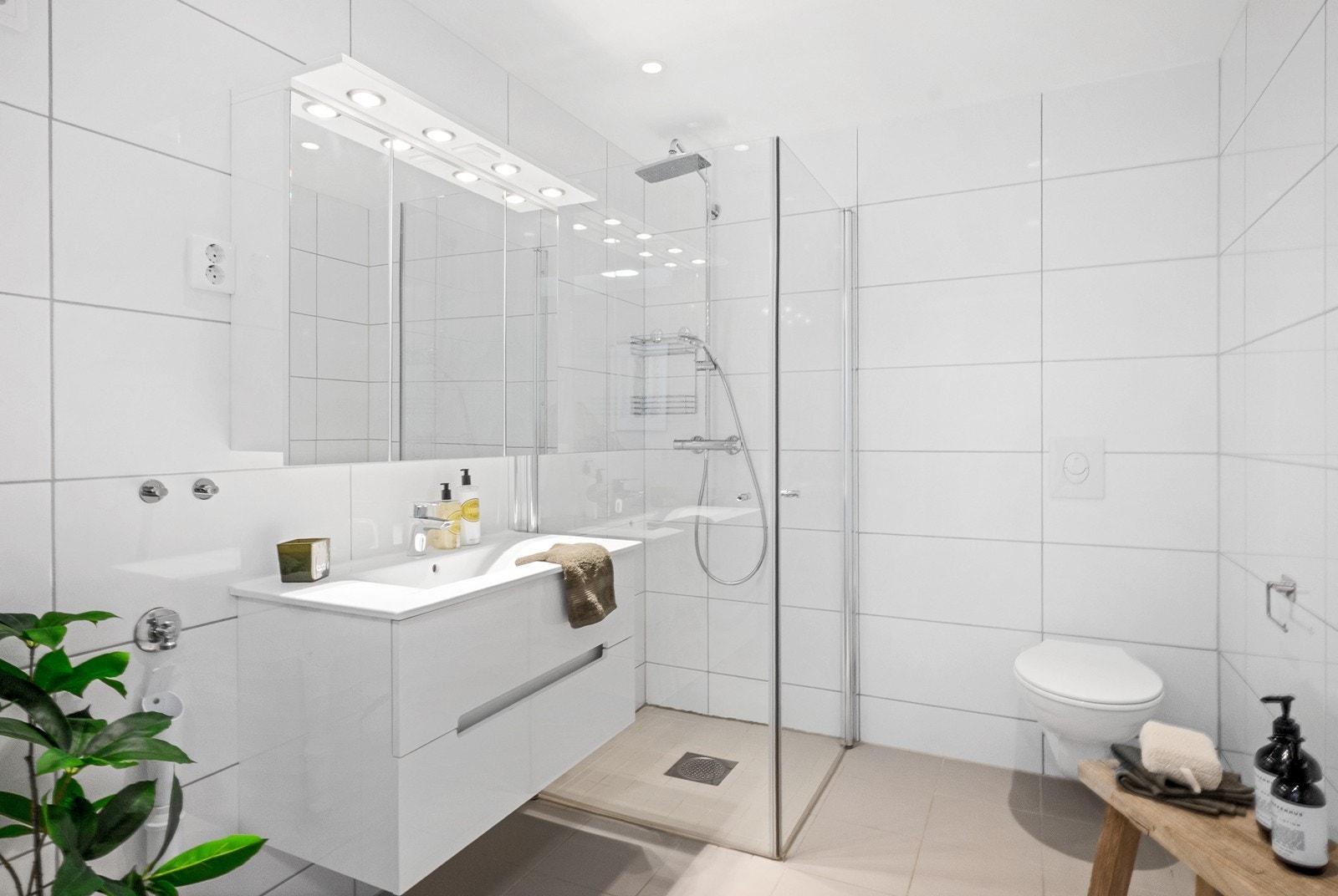 Badet fremstår delikat og tidløst med flislagte overflater i hvitt og beige, varmekabler og downlights. Galleribilde