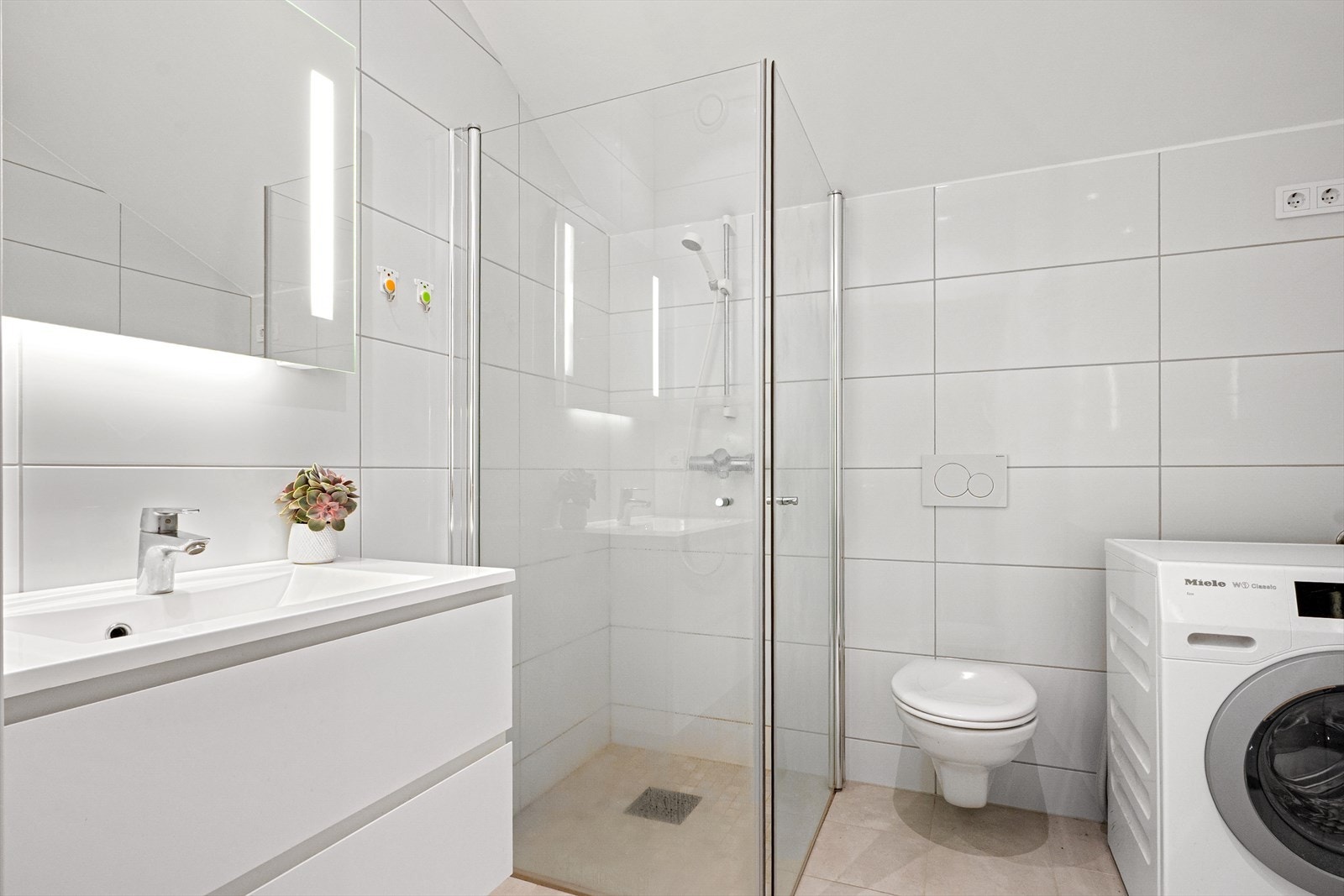 Badet har et pent uttrykk med lyse fliser, gulvvarme og downlights. Galleribilde