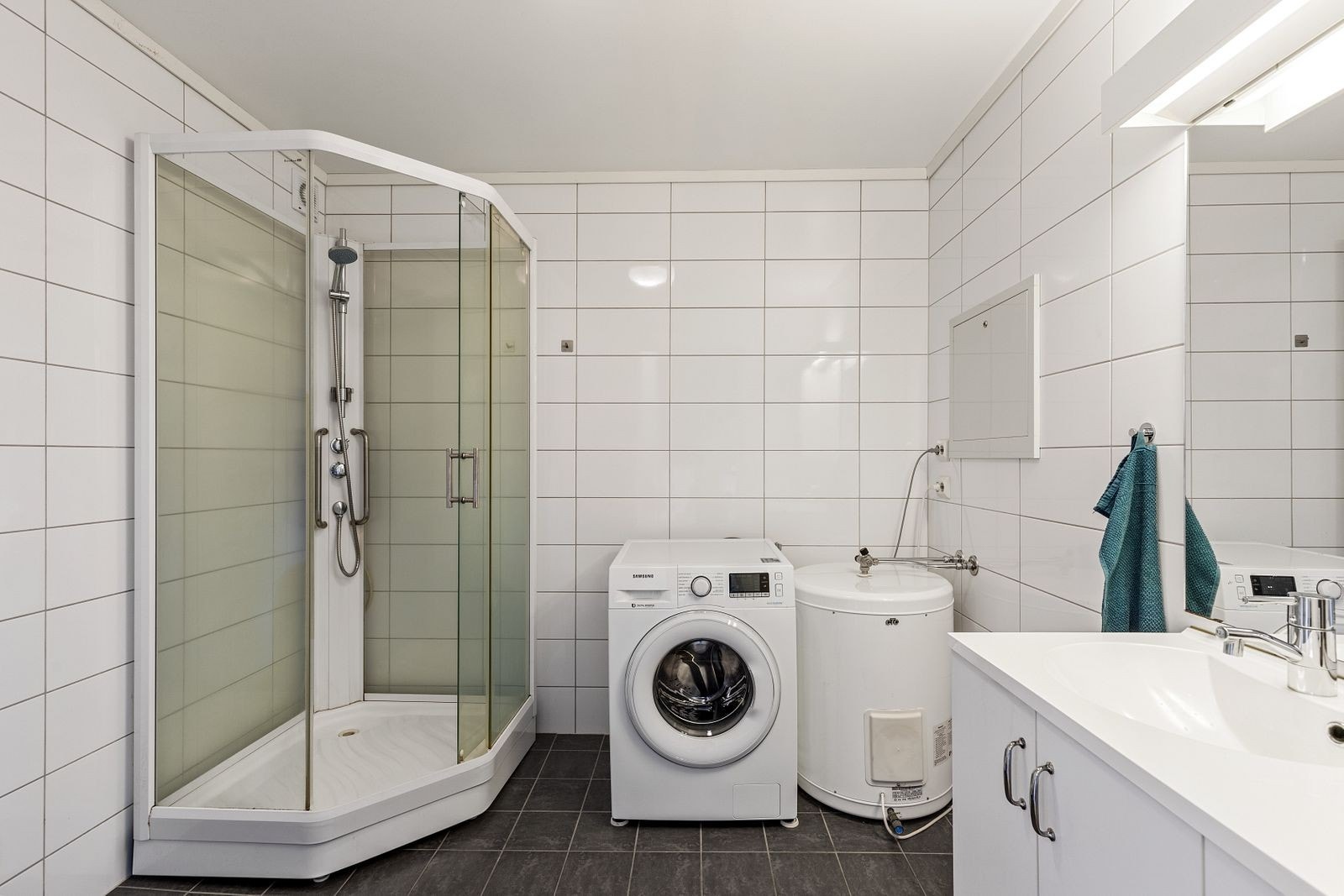 Et hyggelig bad med hvite fliser på veggene og grå fliser på gulvet. Opplegg for vaskemaskin. Galleribilde