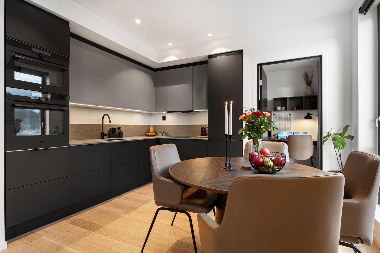 Stilren kjøkkeninnredning med mørke, slette fronter og takhøye overskap i en lysere fargetone Galleribilde