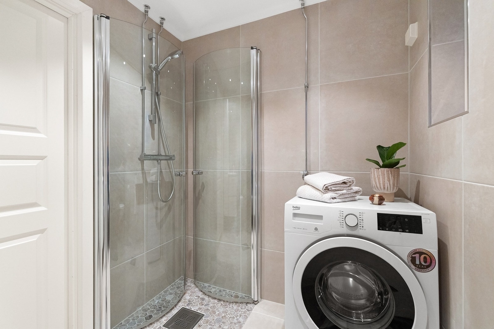 Dusjhjørne med innfellbare glassdører og dusjarmatur tilkoblet hånddusj, vegghengt toalett og opplegg for vaskemaskin Galleribilde